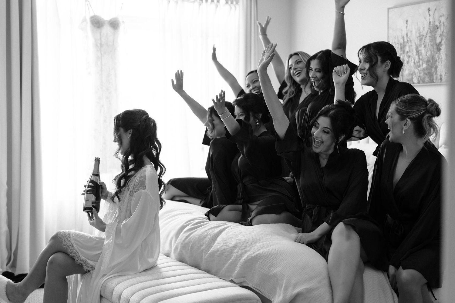 Large group of formally dressed people gathered in a bright room with white curtains for a special occasion.
