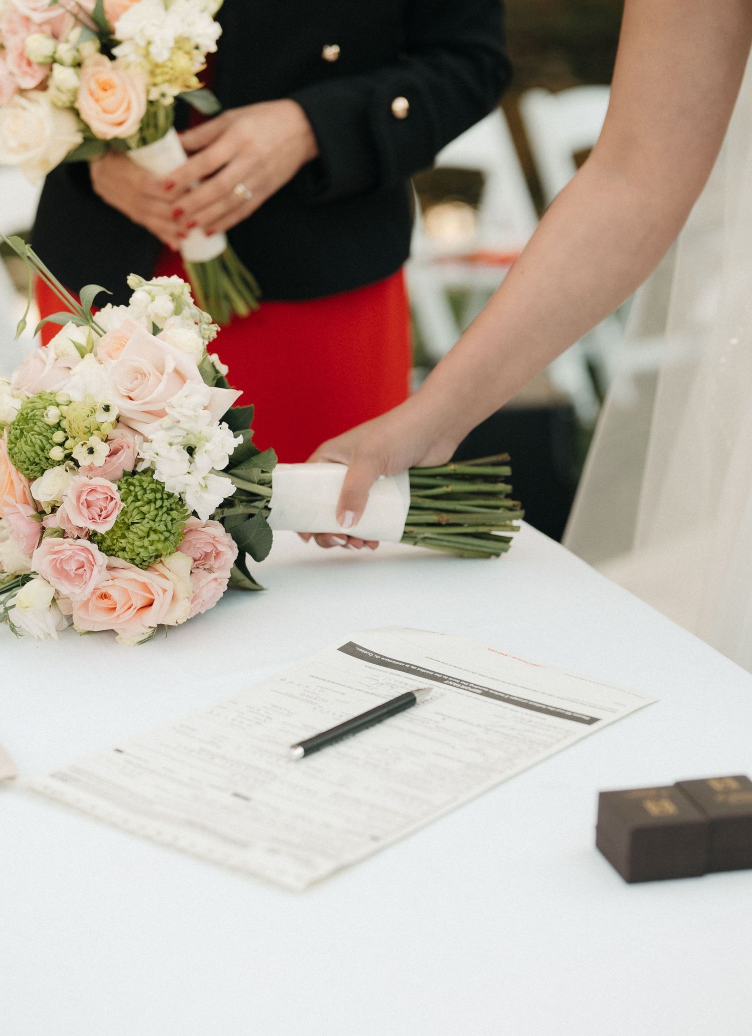 Wedding ceremony details with pink roses and paperwork being signed on a white table.