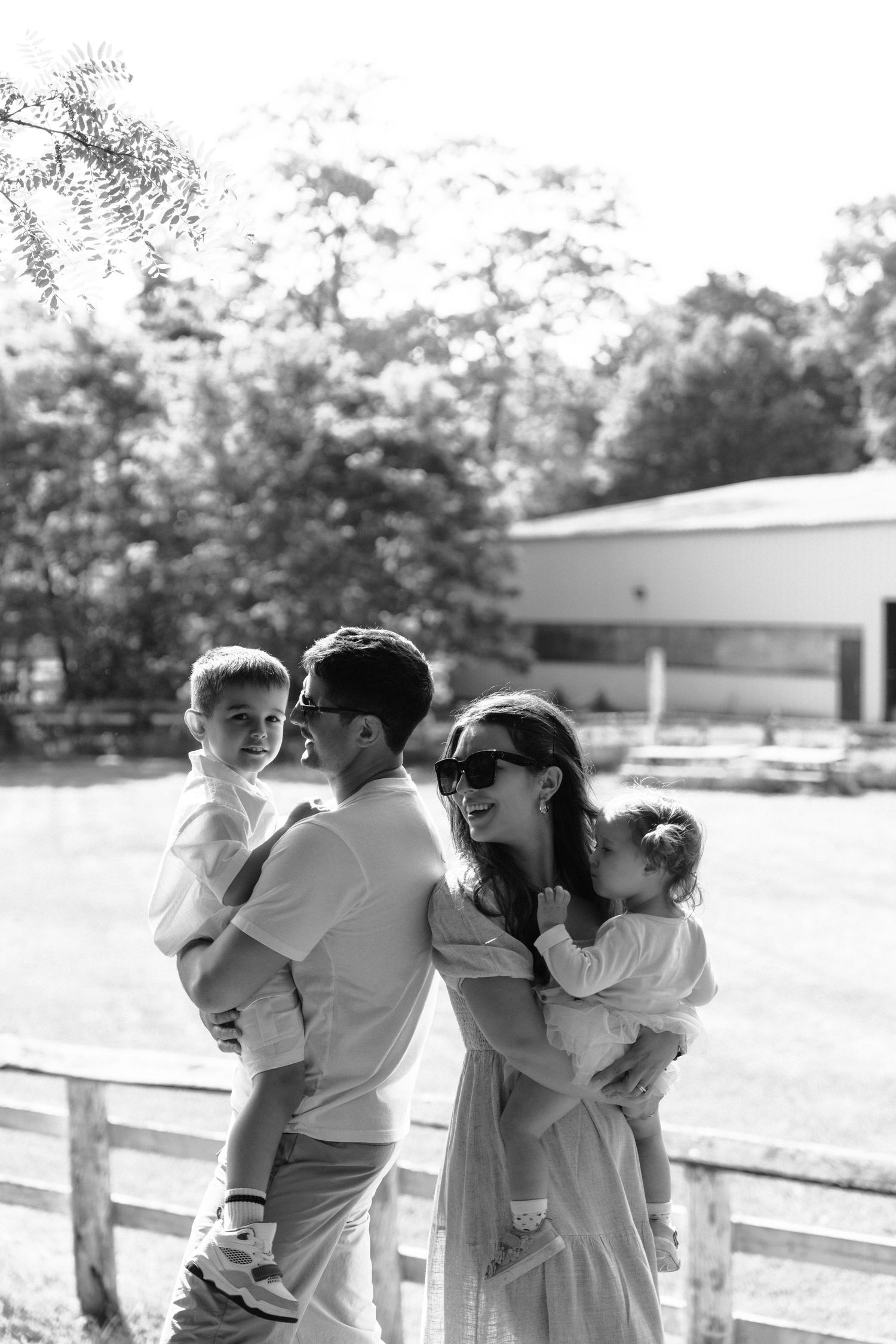 A family enjoys a black and white moment together on a sunny day near a wooden fence.