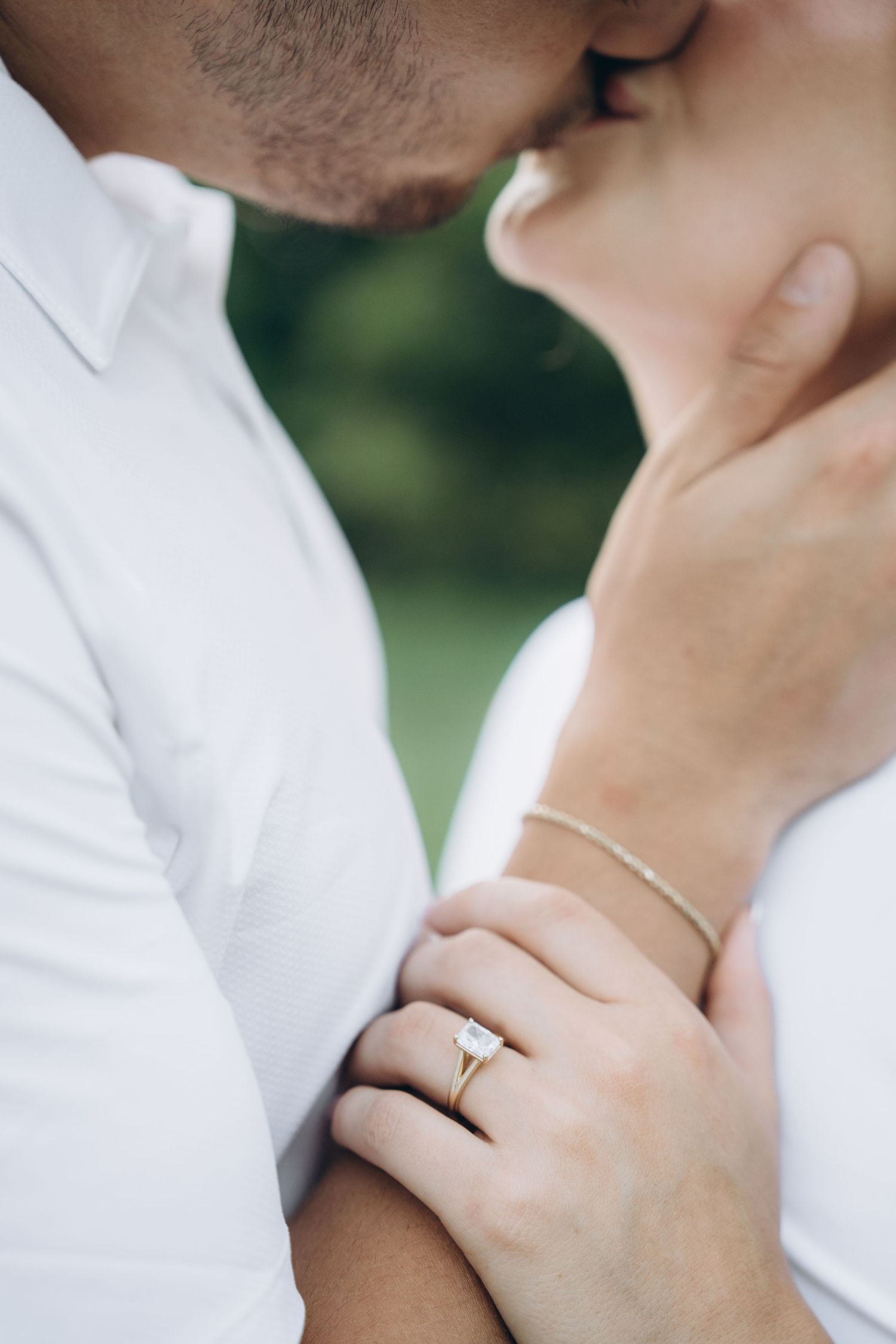 A romantic close-up photo of a couple kissing with focus on an engagement ring and delicate bracelet.