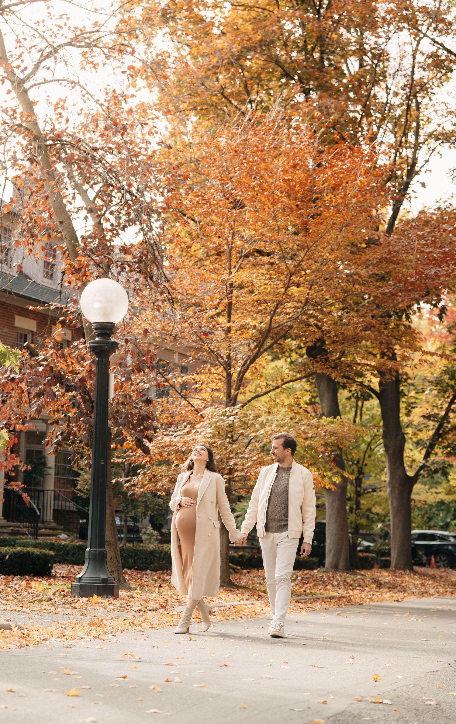 People walking along tree-lined path with beautiful fall foliage and lamp posts during autumn season.