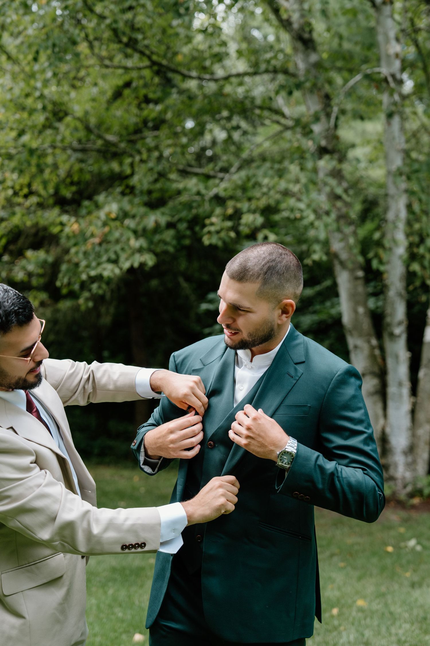 Two men in formal attire playfully spar with each other in a park setting with trees in the background.