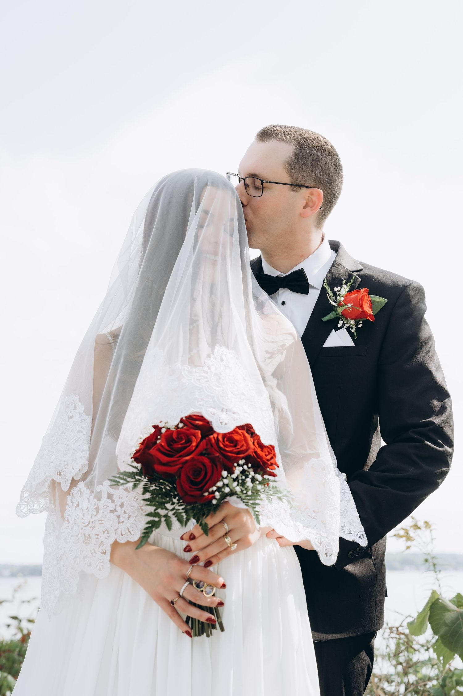Close-up wedding photography series shows couple with classic veil details and vibrant red rose bouquet against white backdrop.
