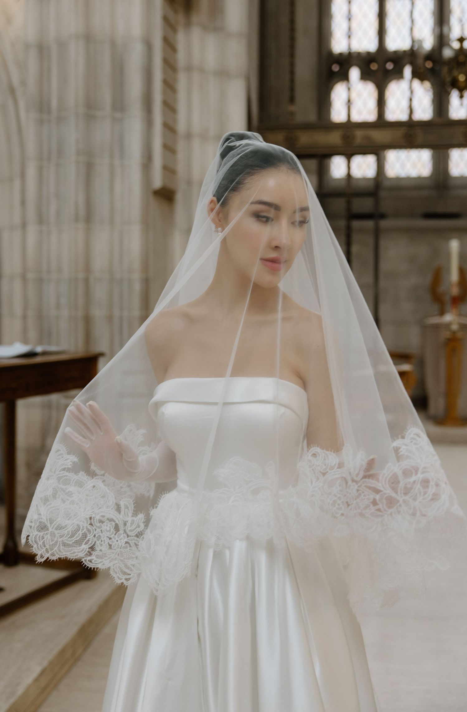 Beautiful bridal portrait in a church featuring a classic strapless white wedding gown and delicate lace-trimmed veil.