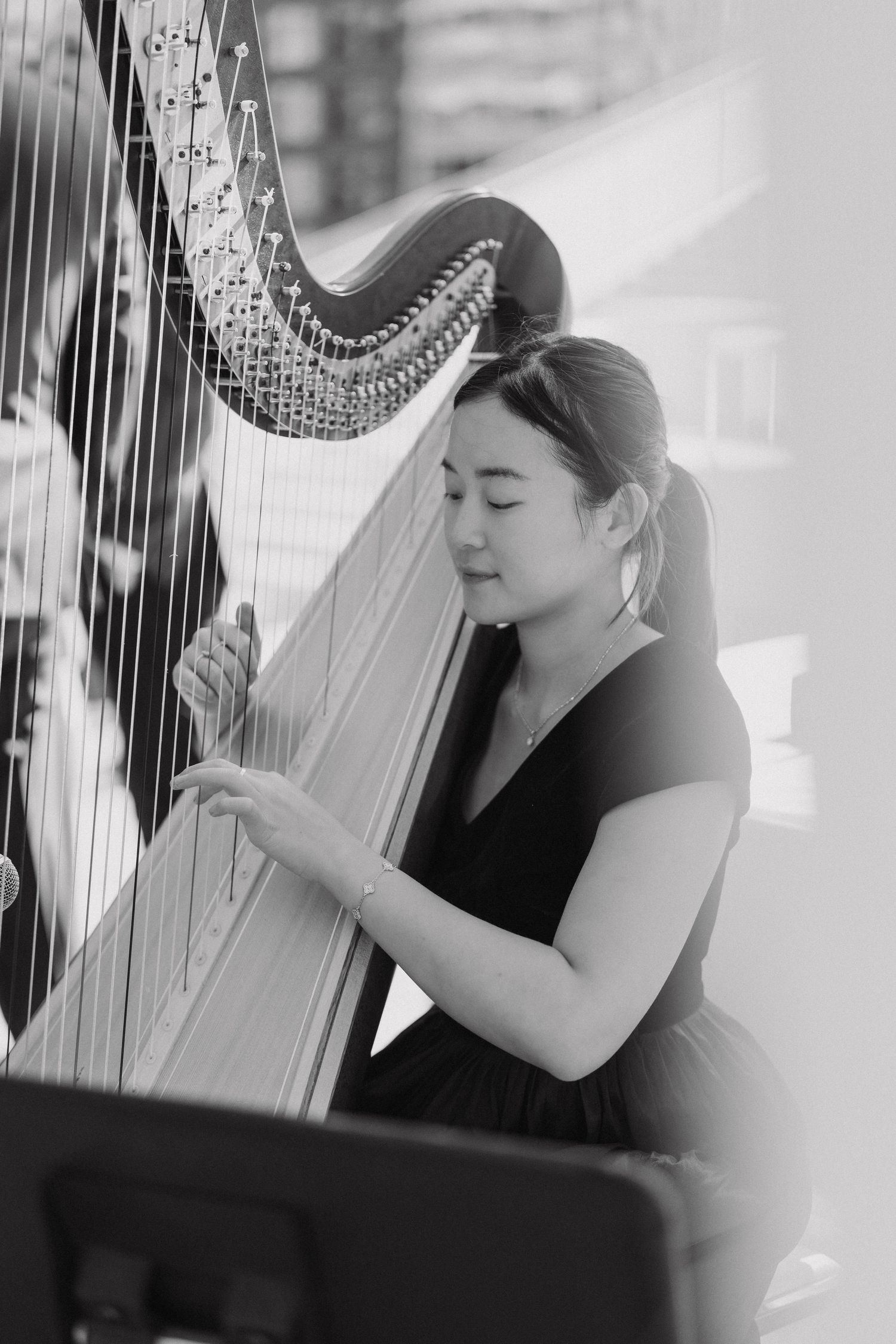 A musician in a black dress plays a classical harp during a performance in black and white photography.