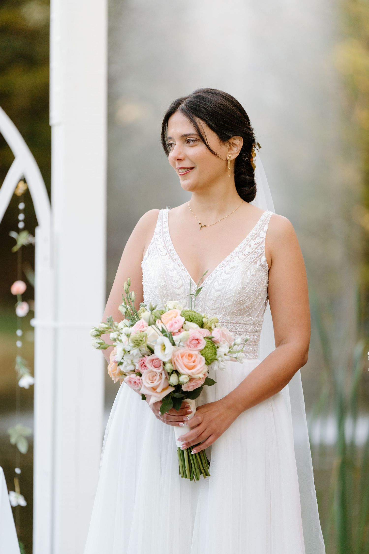 Wedding portrait in front of white arch with pink and white bouquet.