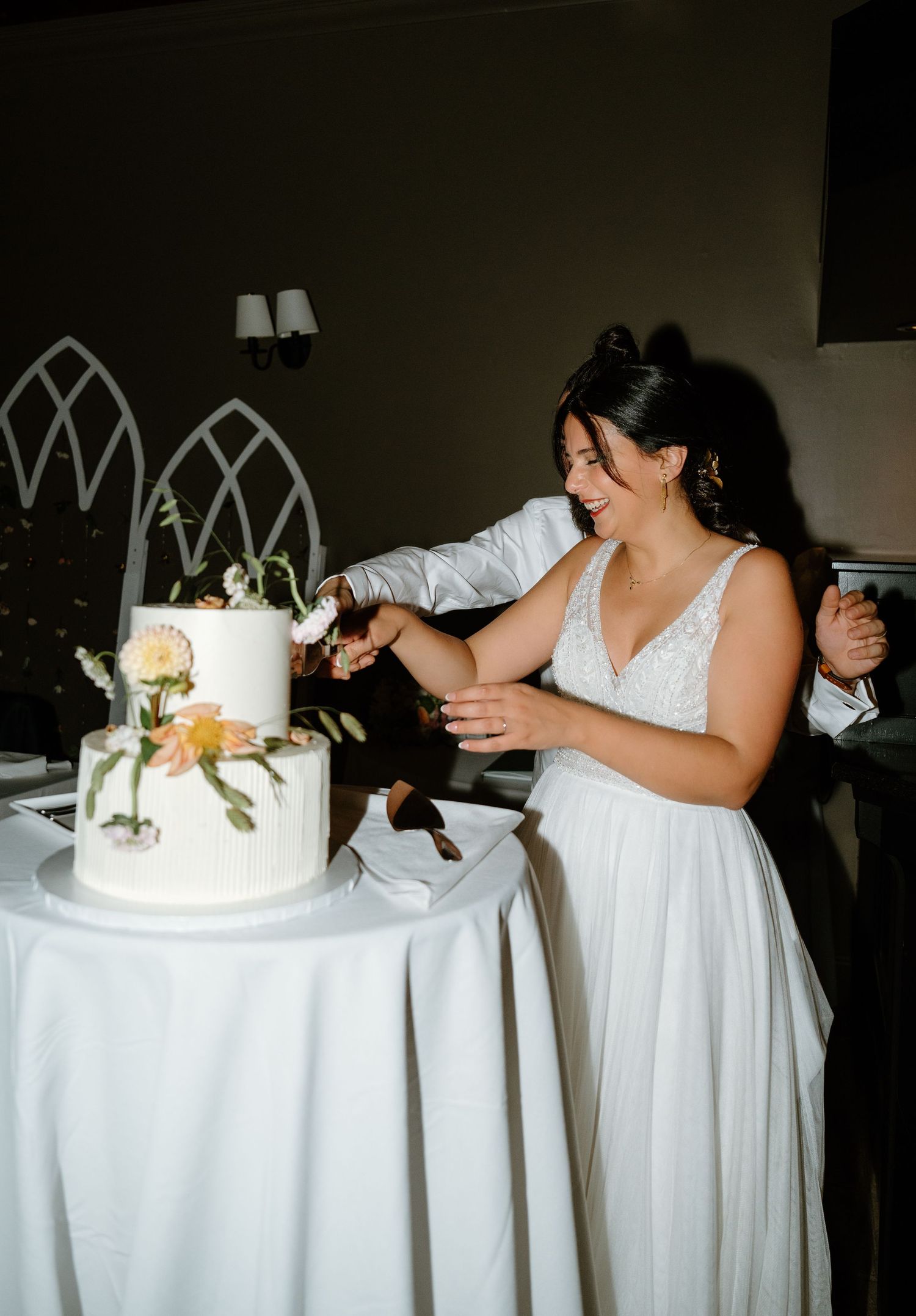 A couple cuts their elegant two-tier white wedding cake decorated with floral accents during their reception.