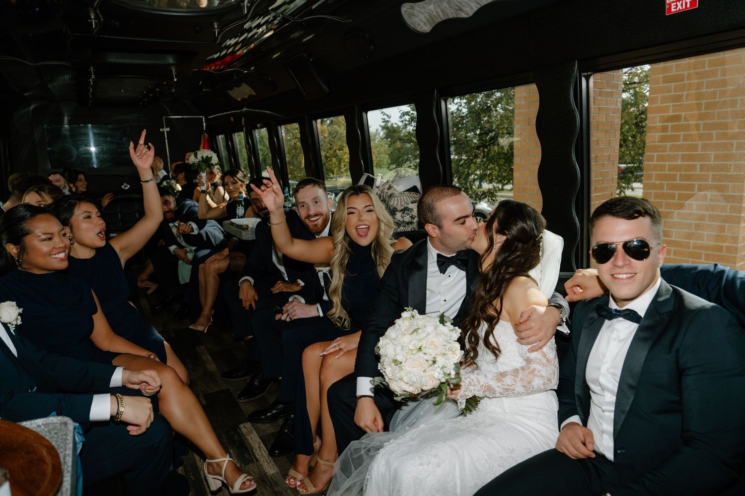 Wedding party celebrating and having fun while riding together on a party bus with bouquets and formal attire.