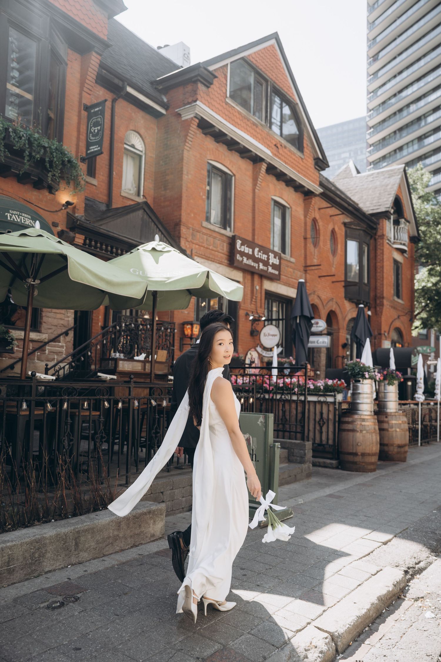 A white dress on a street near historic brick buildings with outdoor patio seating and wine barrels in Yorkville, Toronto.