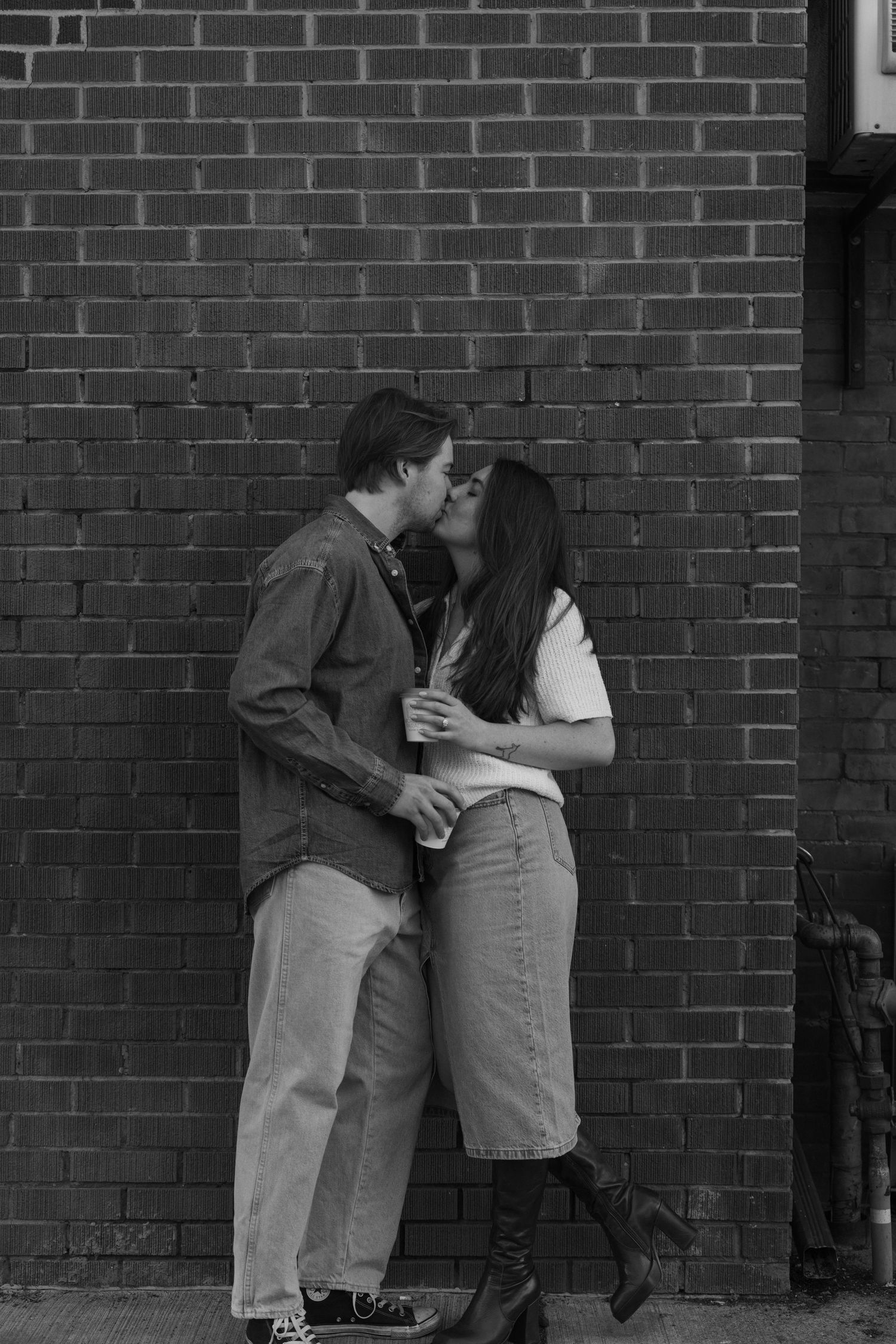 A romantic black and white photo of a couple embracing against a brick wall.
