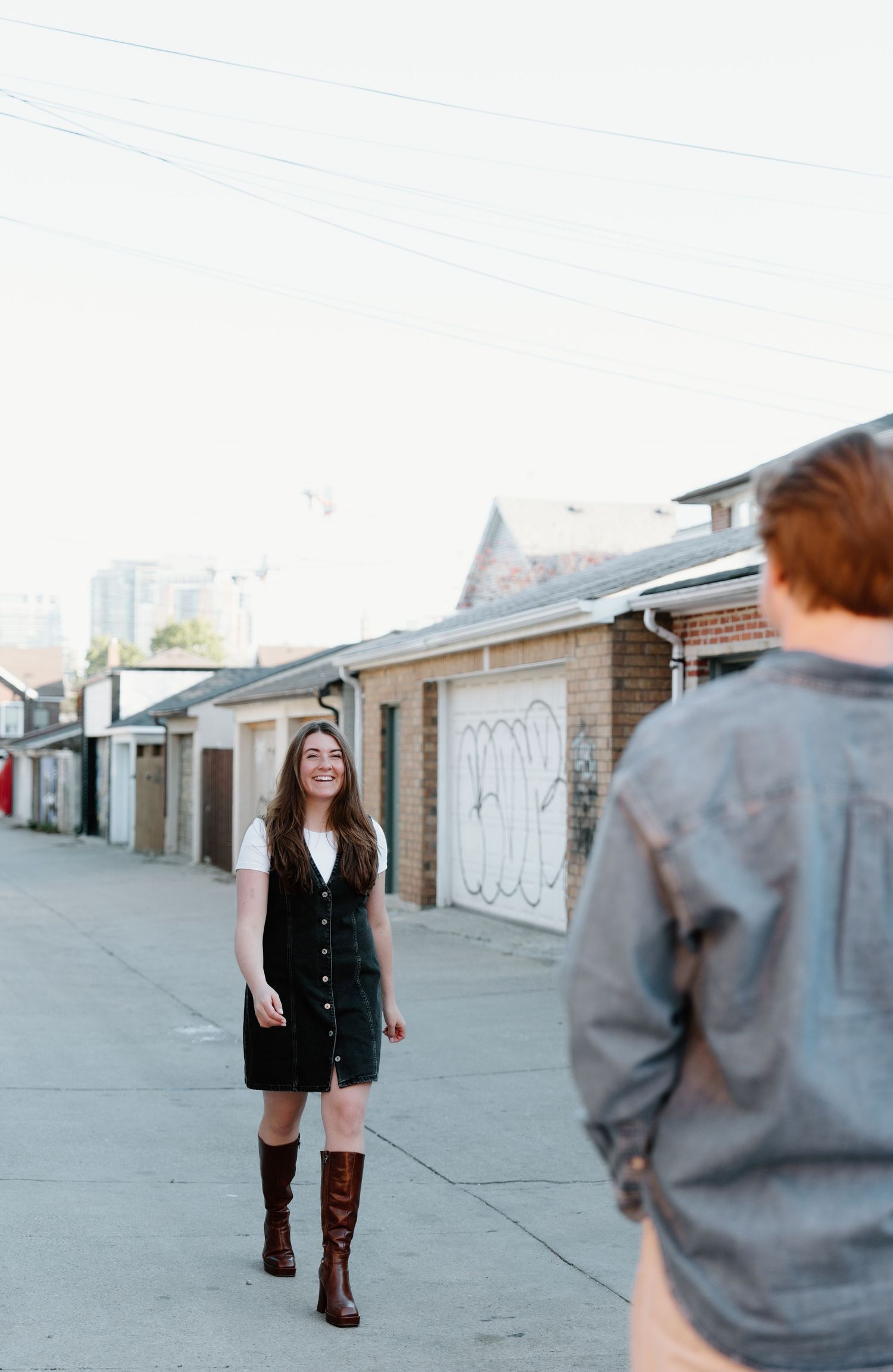 Two people stand in an urban alley with garages and buildings in the background on a bright day.