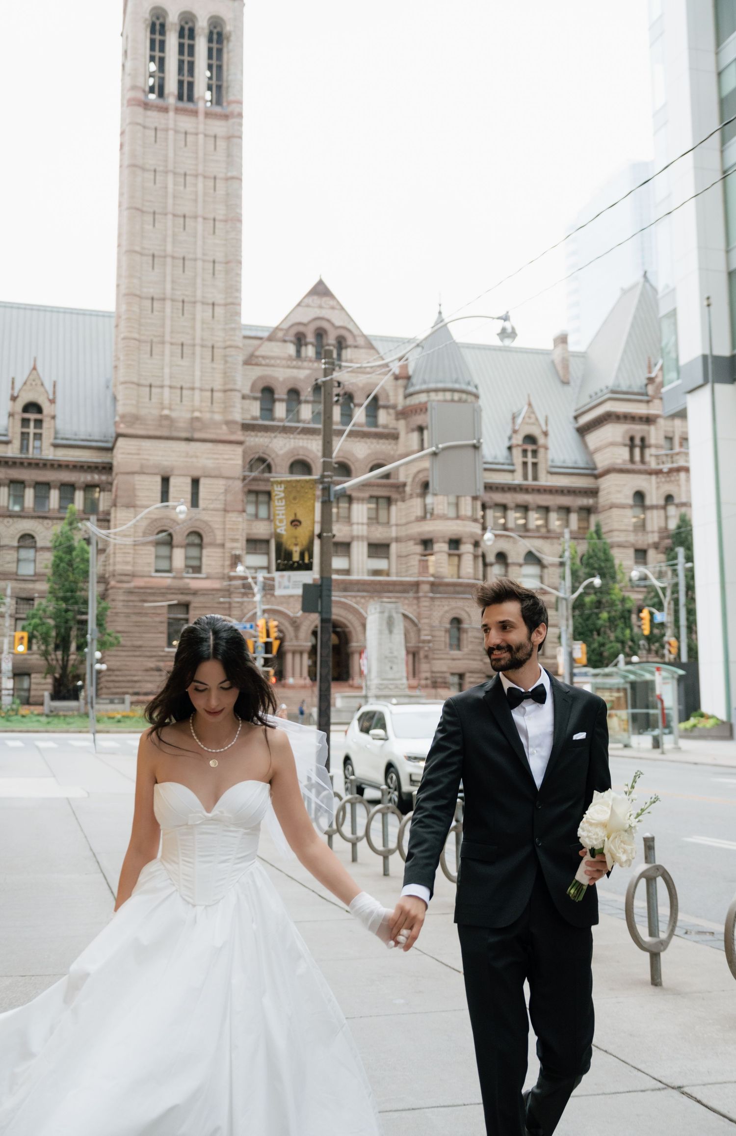 A wedding couple strolls in front of the Romanesque architecture of Toronto's Old City Hall.