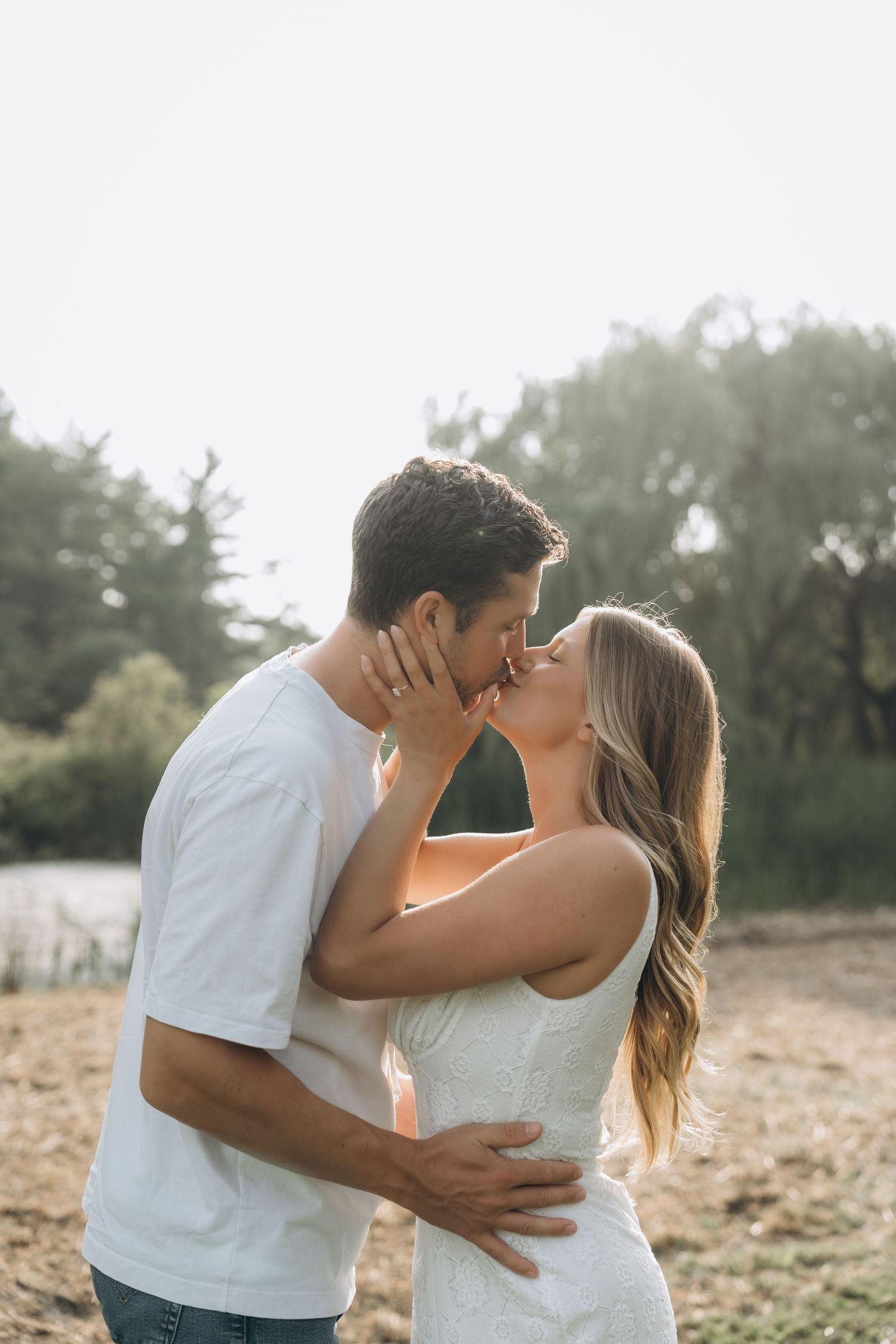A romantic couple in white outfits sharing tender moments together in a sunlit outdoor setting.