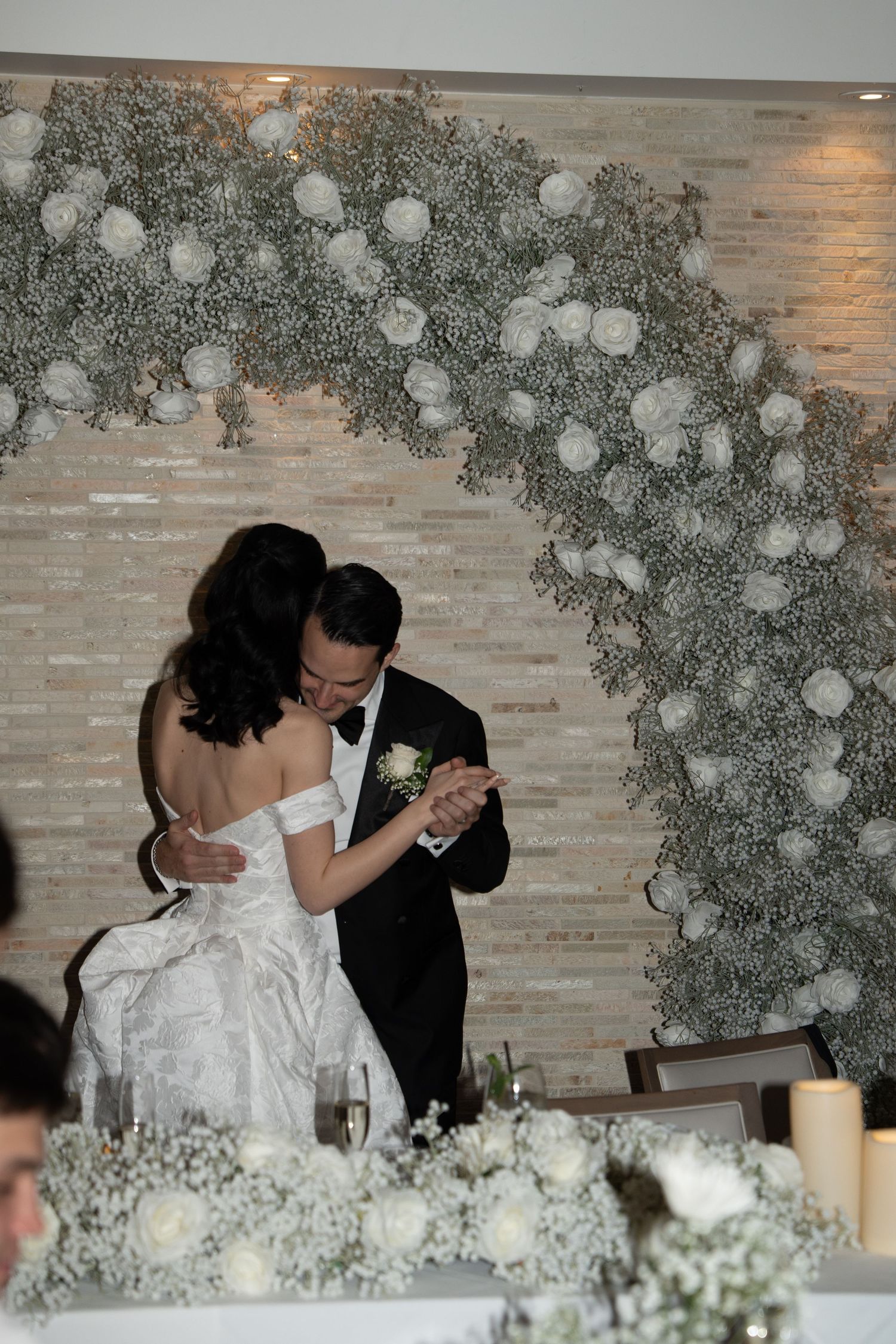 A romantic wedding moment under an elegant baby's breath floral arch with white roses and candlelit table decor.