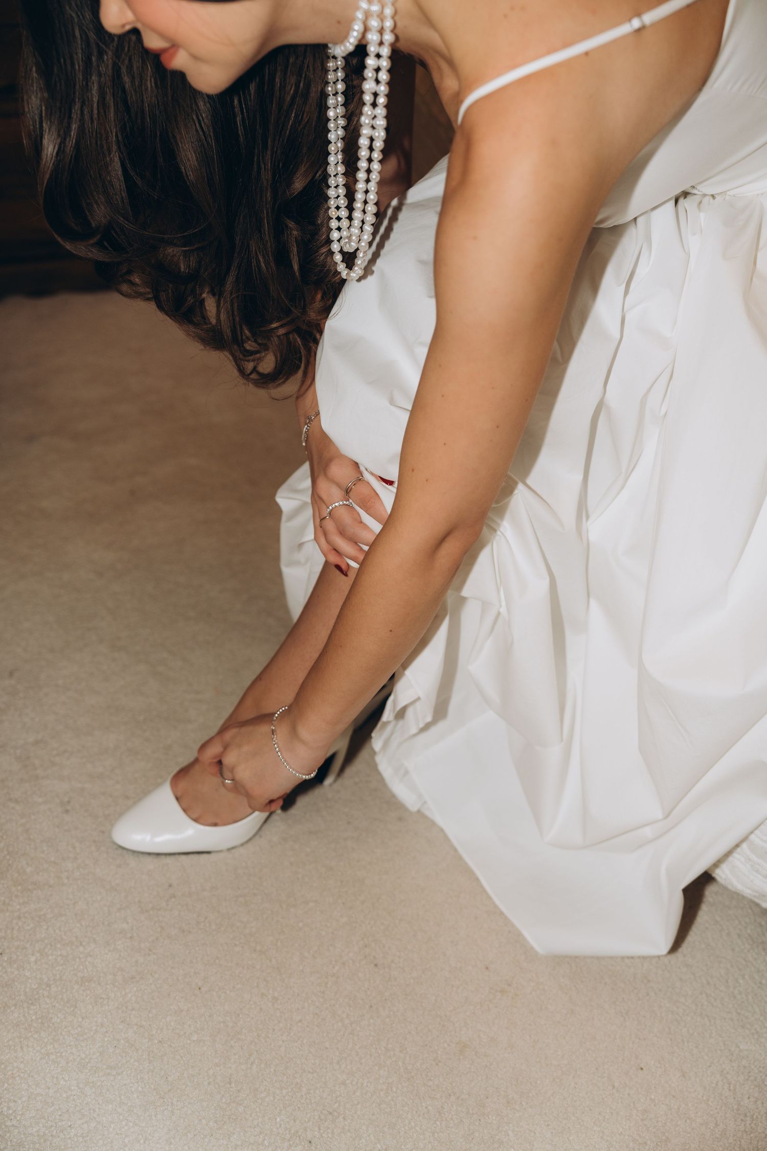 Close-up sequence of a bride putting on white ballet flats while wearing a pearl necklace and wedding dress.