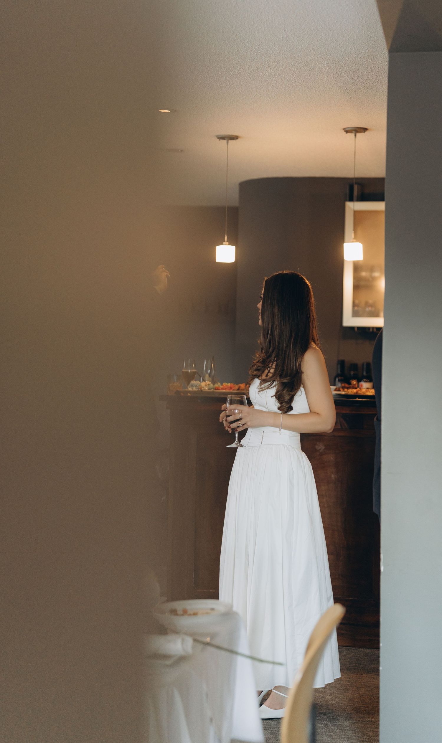 A person in a white summer dress walks through a modern apartment interior with pendant lighting.