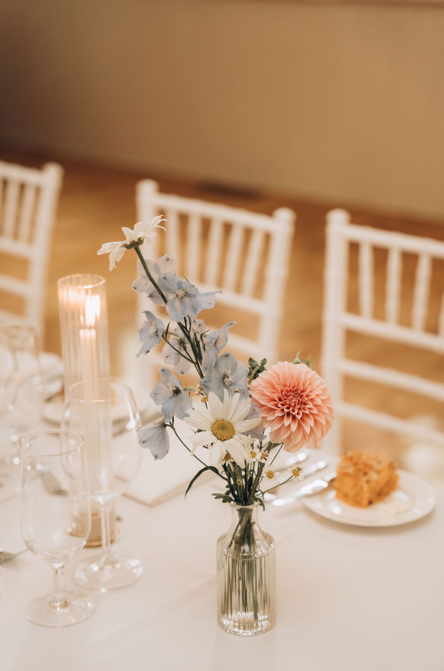 Elegant wedding table setting with delicate pink and white floral centerpieces in glass vases and white chairs.