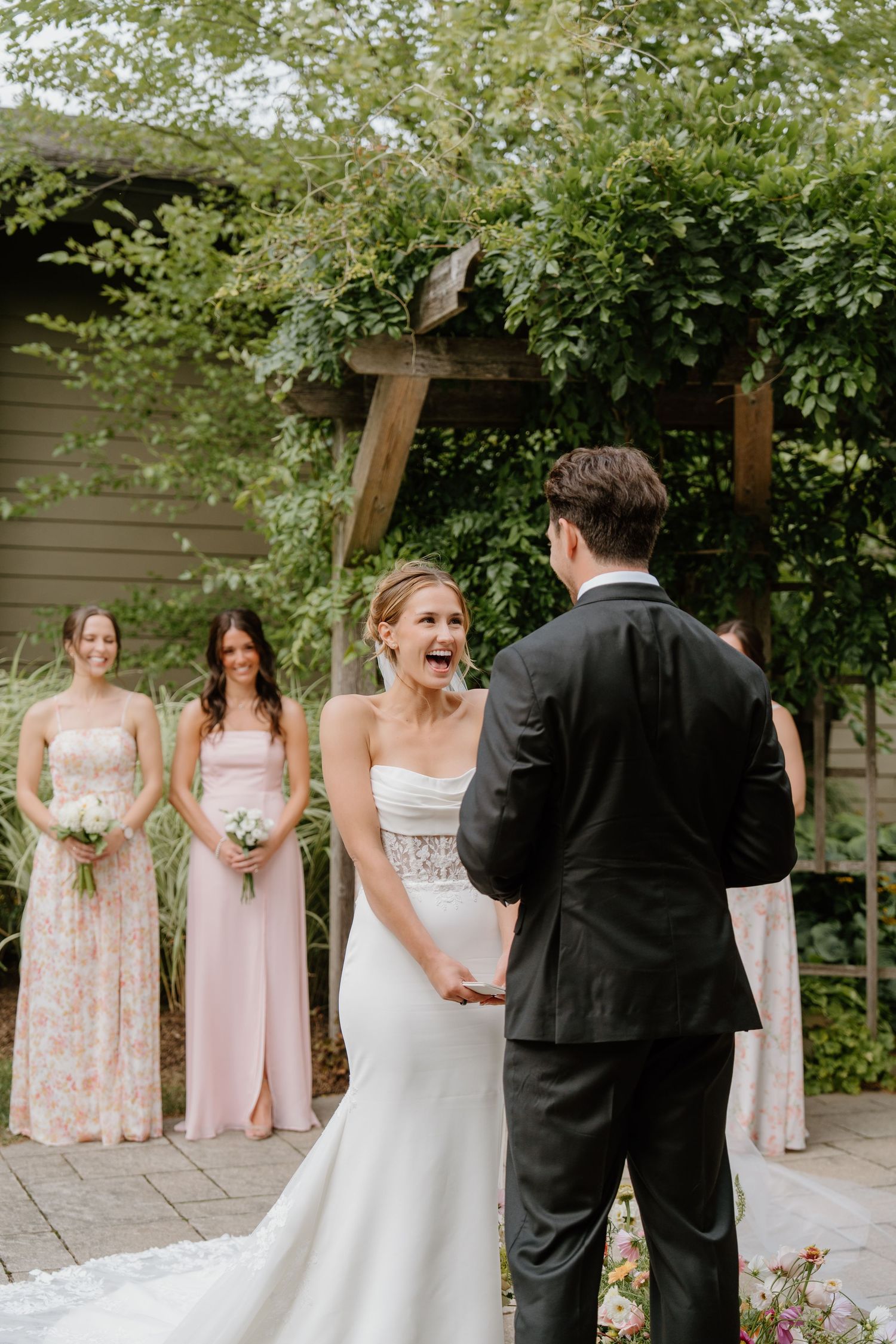 Wedding party stands outdoors in formal attire with bridesmaids in pink dresses and couple in black and white.