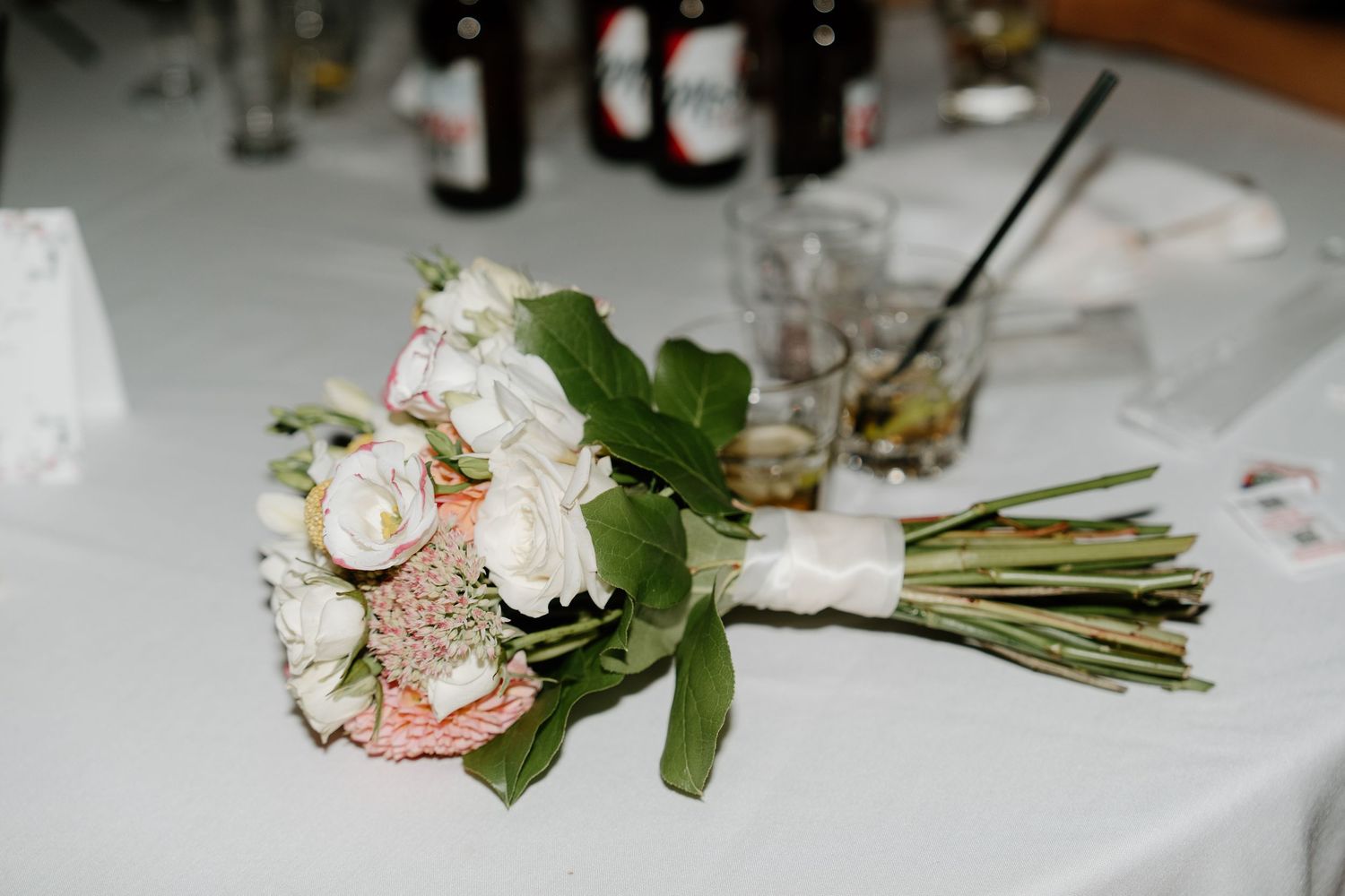 Wedding reception tables decorated with elegant floral centerpieces, wine bottles, and white linens.