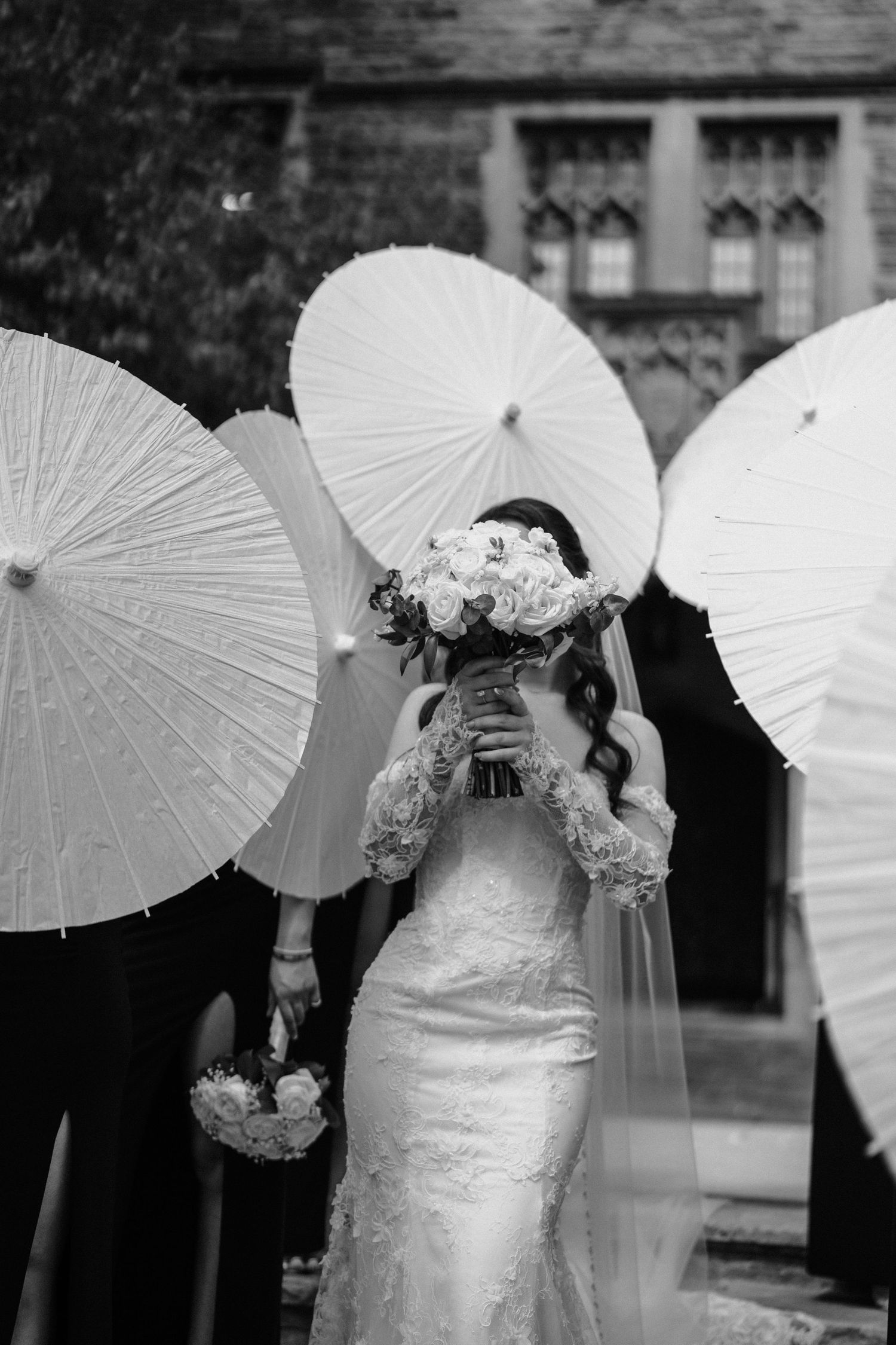 Wedding party poses with elegant white paper parasols creating a romantic black and white photograph.