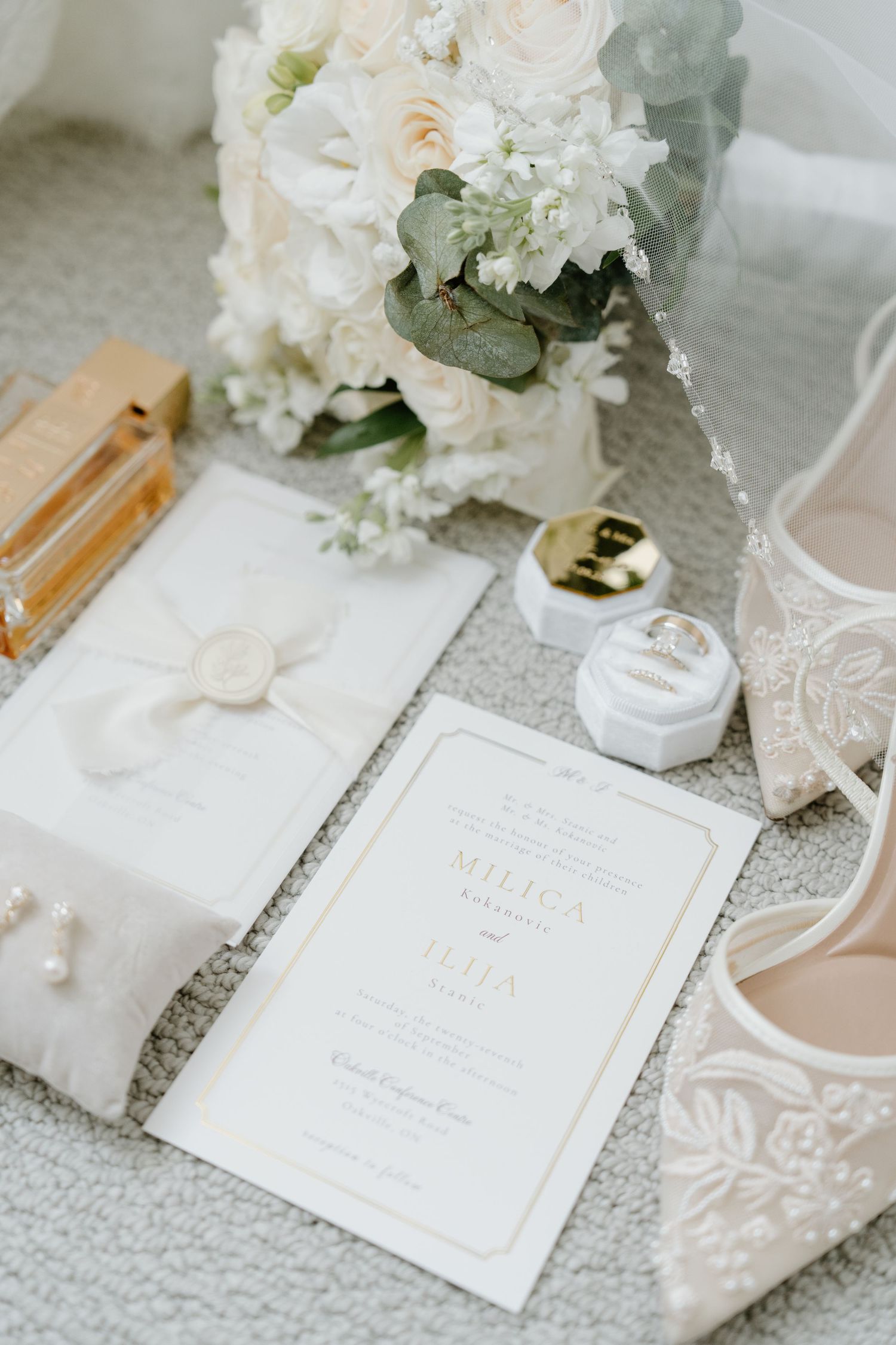 Elegant white wedding invitation suite with floral arrangements and delicate lace details on a light gray textured surface.