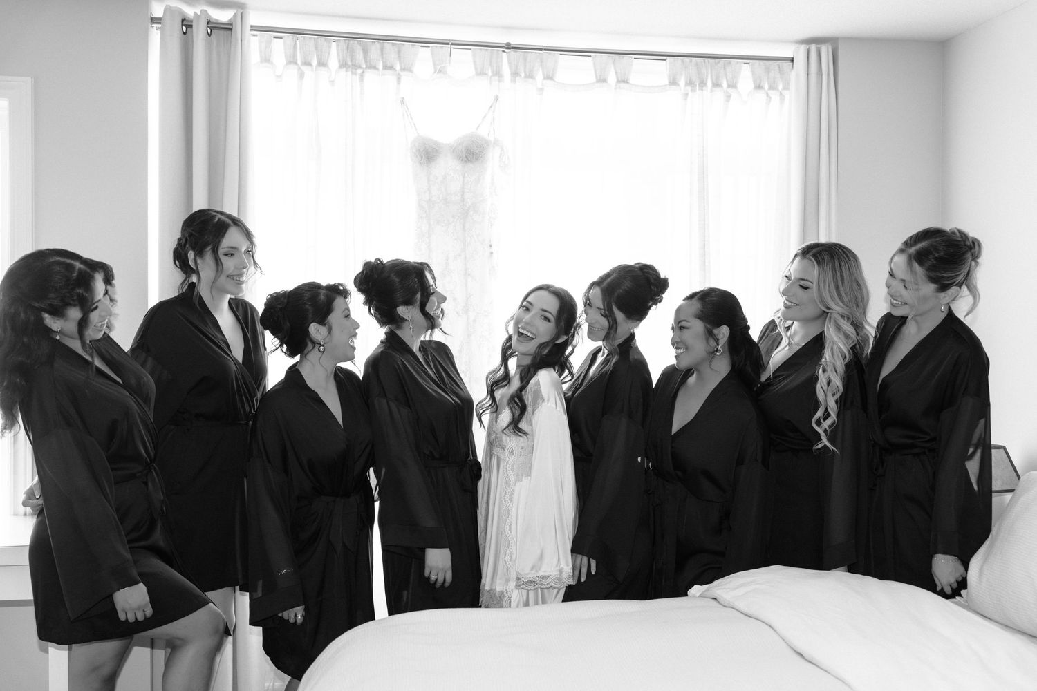 Wedding guests mingling in an elegant white room with natural light streaming through sheer curtains.
