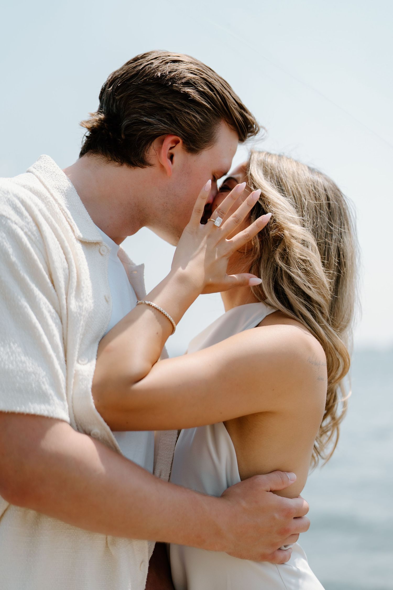 A romantic couple in light summer clothing sharing an intimate kiss by the ocean.