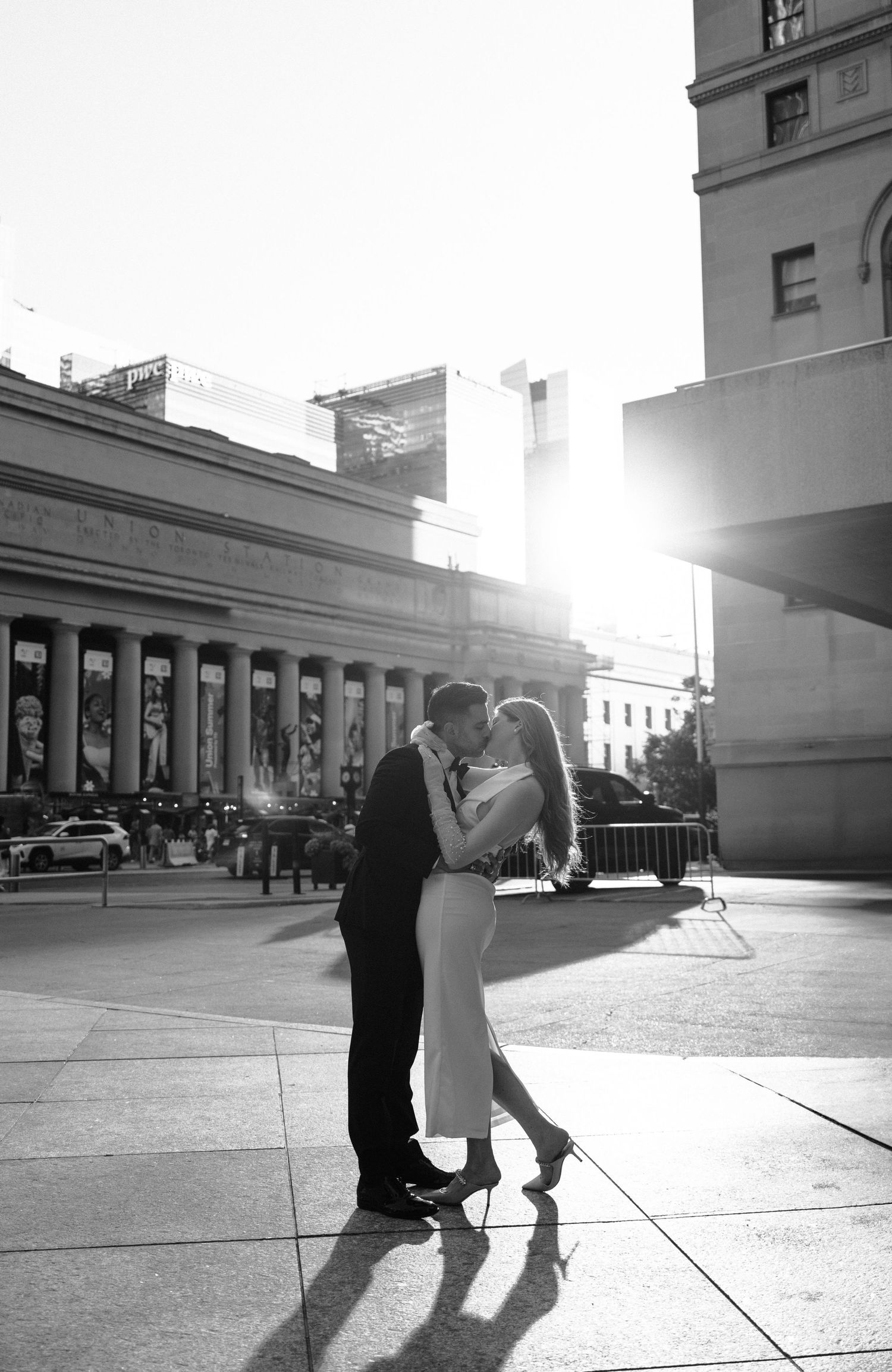 A romantic couple dances gracefully in silhouette outside a historic building façade during a bright sunny afternoon.