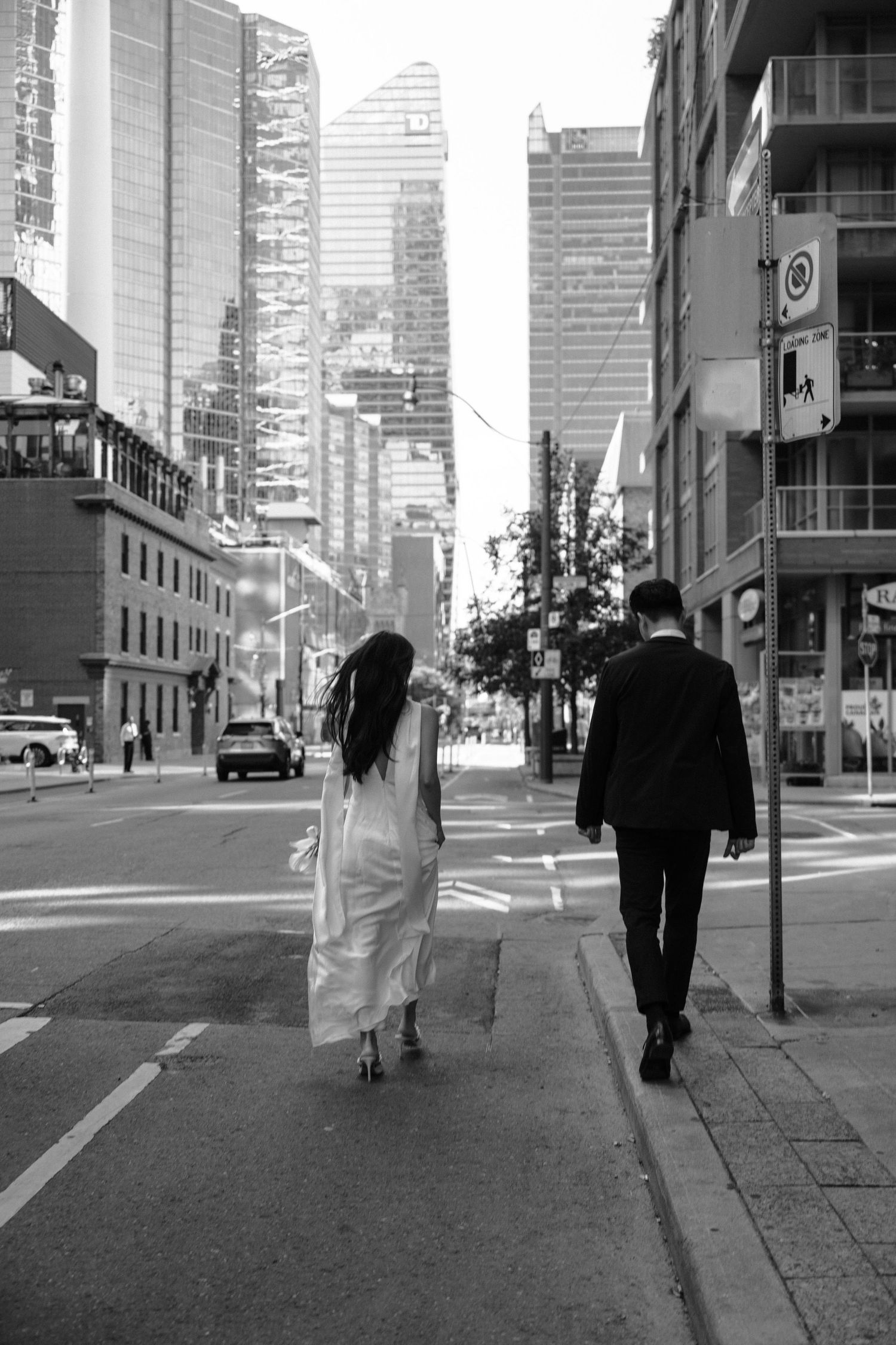 A black and white urban street scene with two people walking past high-rise buildings in a city downtown area.
