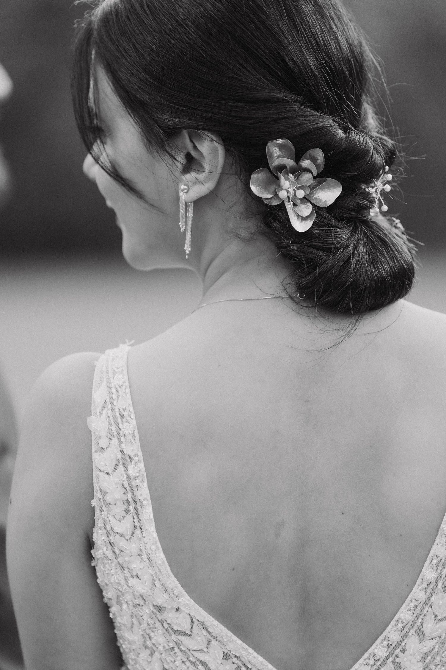 Back view of bride's hairstyle with floral accessory and lace dress detail.