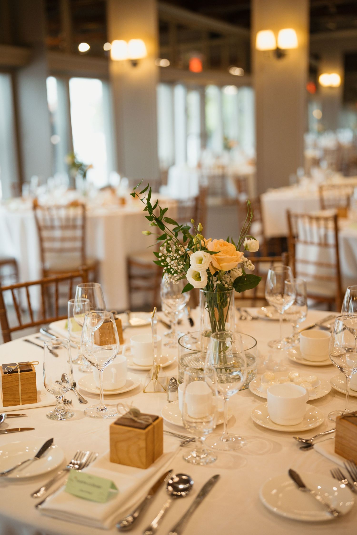 Elegant table setting with wooden favor boxes, crystal glassware, and fresh floral arrangements.