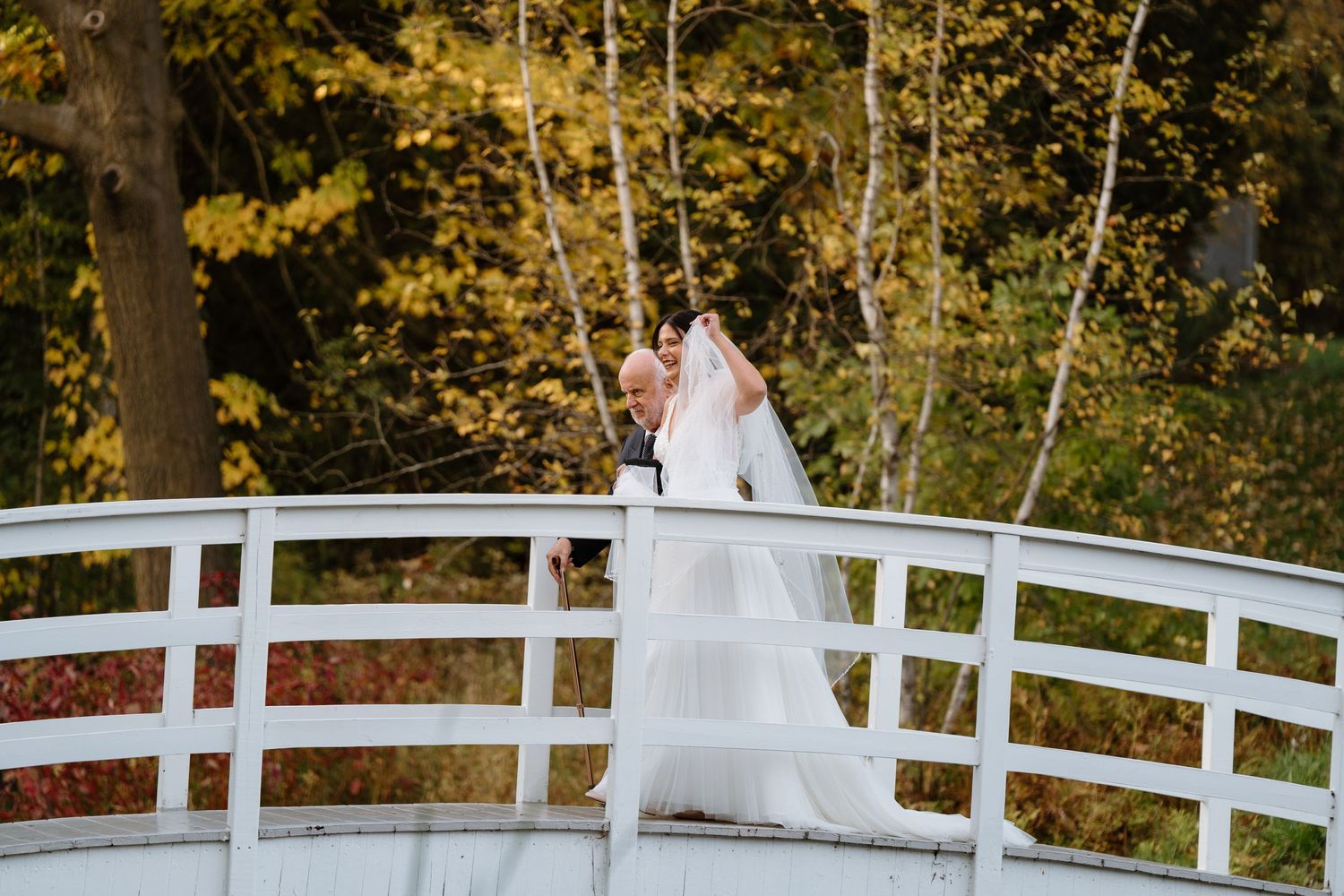 Wedding couple on white bridge surrounded by autumn foliage.