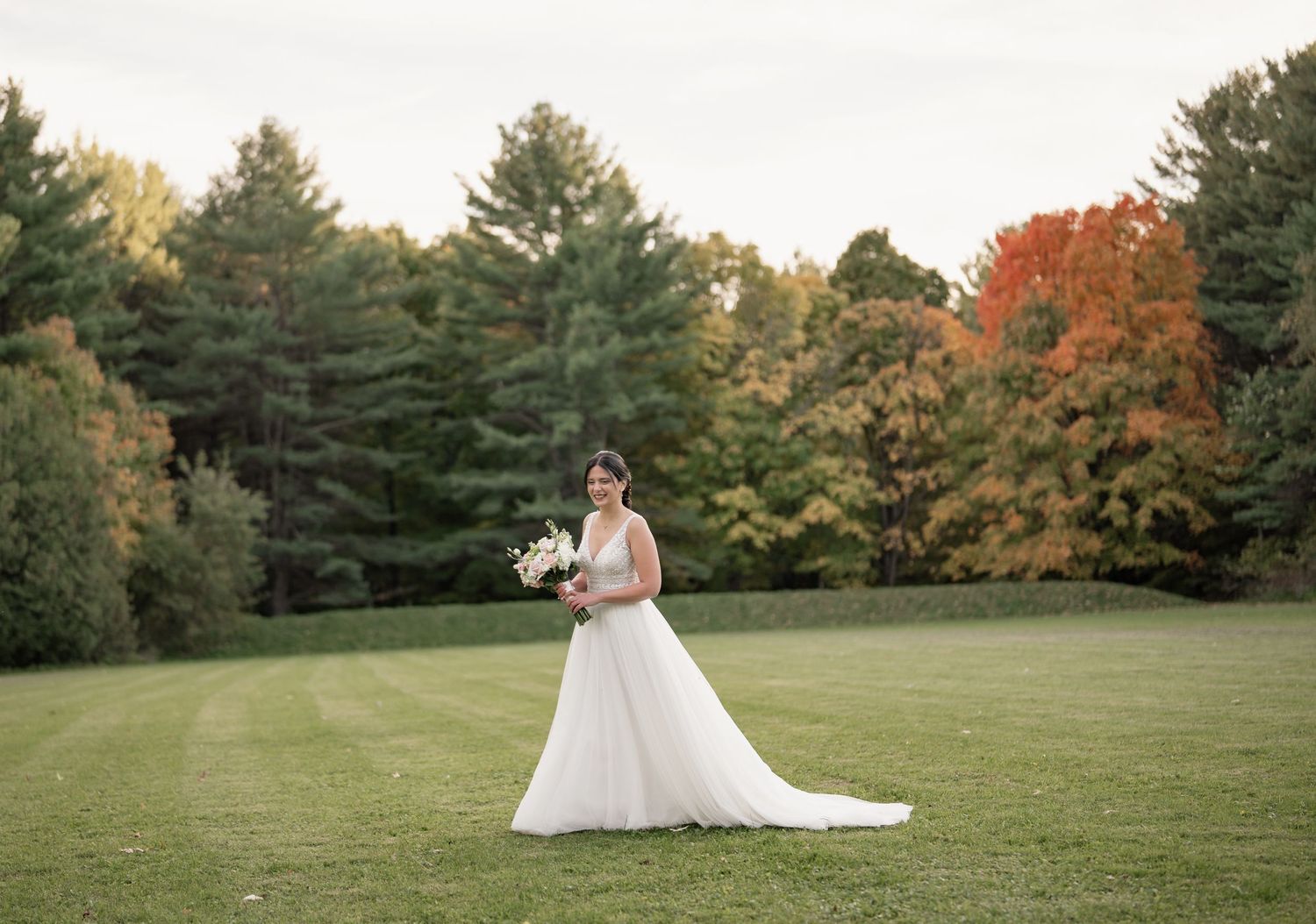 Wedding portrait showcasing a flowing white gown against autumn trees and an open meadow.