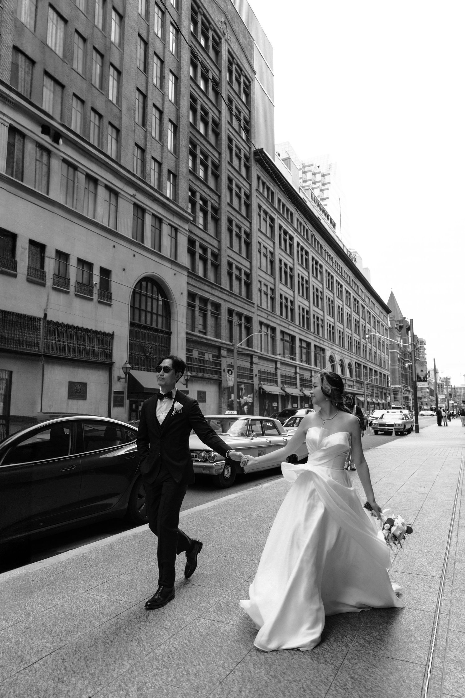 A couple in wedding attire walks along an industrial urban street in a black and white photo series.