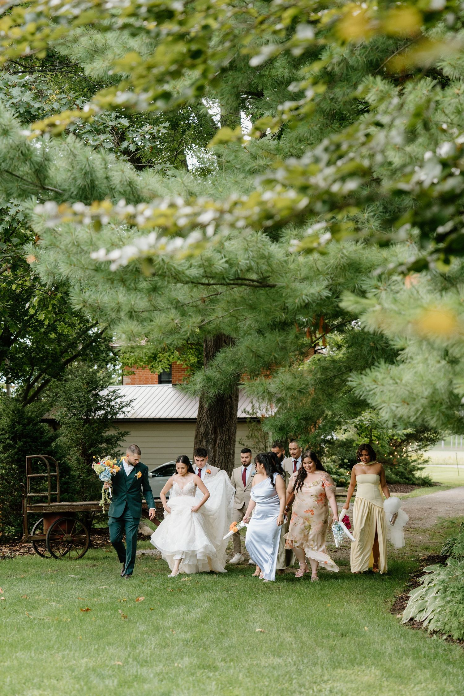 Wedding party walks together through a lush green garden path on a sunny summer day.