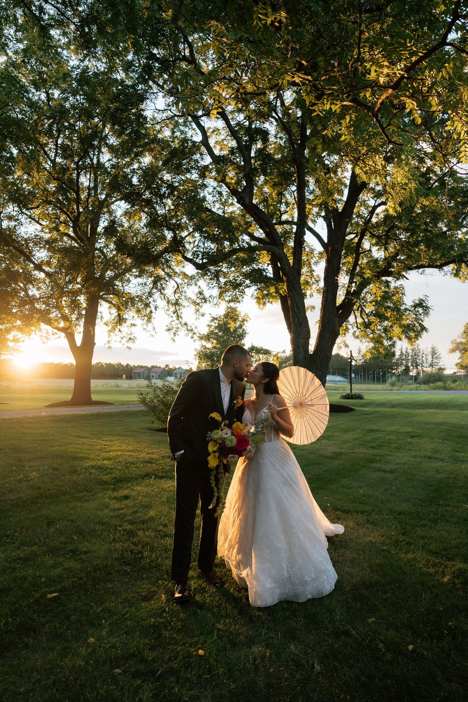 A romantic sunset wedding photo shoot under large trees with golden light filtering through the branches.