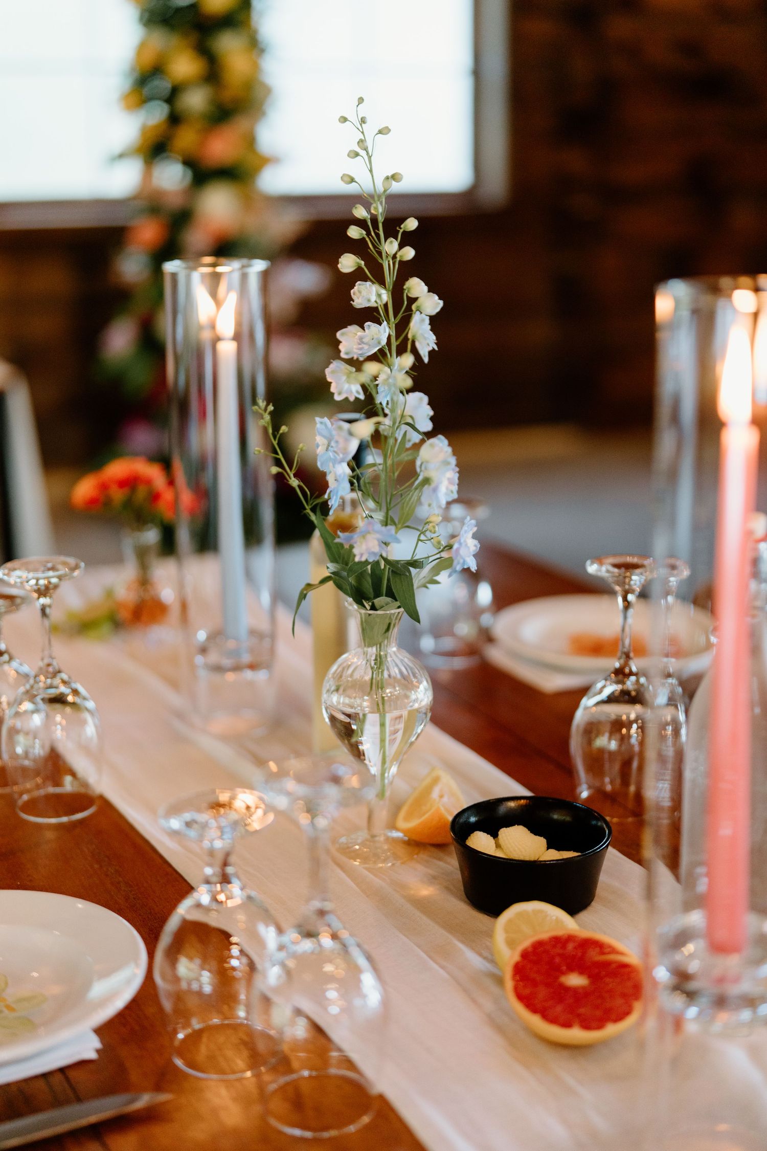 Elegant wedding reception table setting with grapefruit slices, white flowers in vases, and glowing candles.