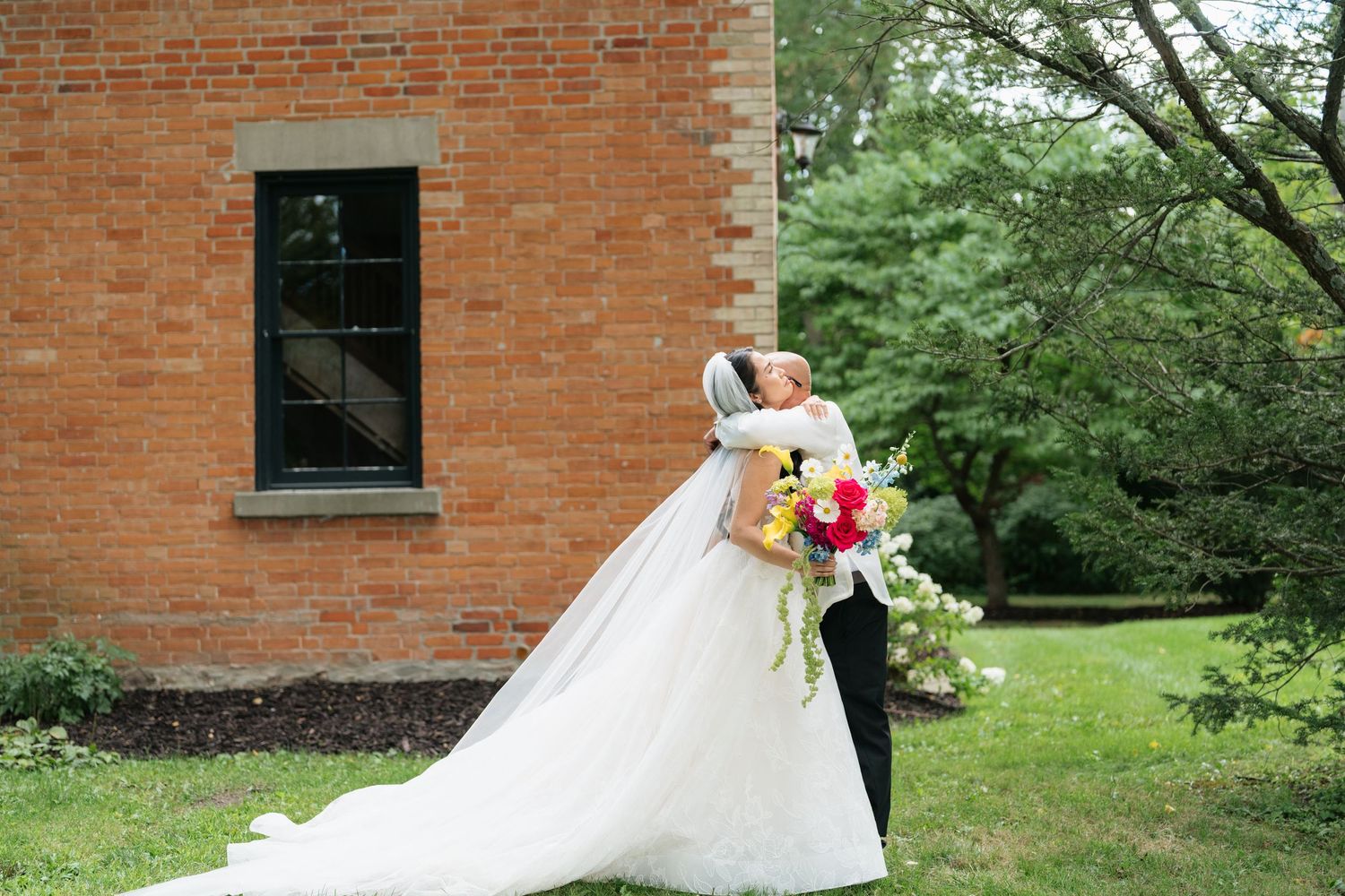 A white wedding dress train trails elegantly across red brick steps surrounded by lush greenery.