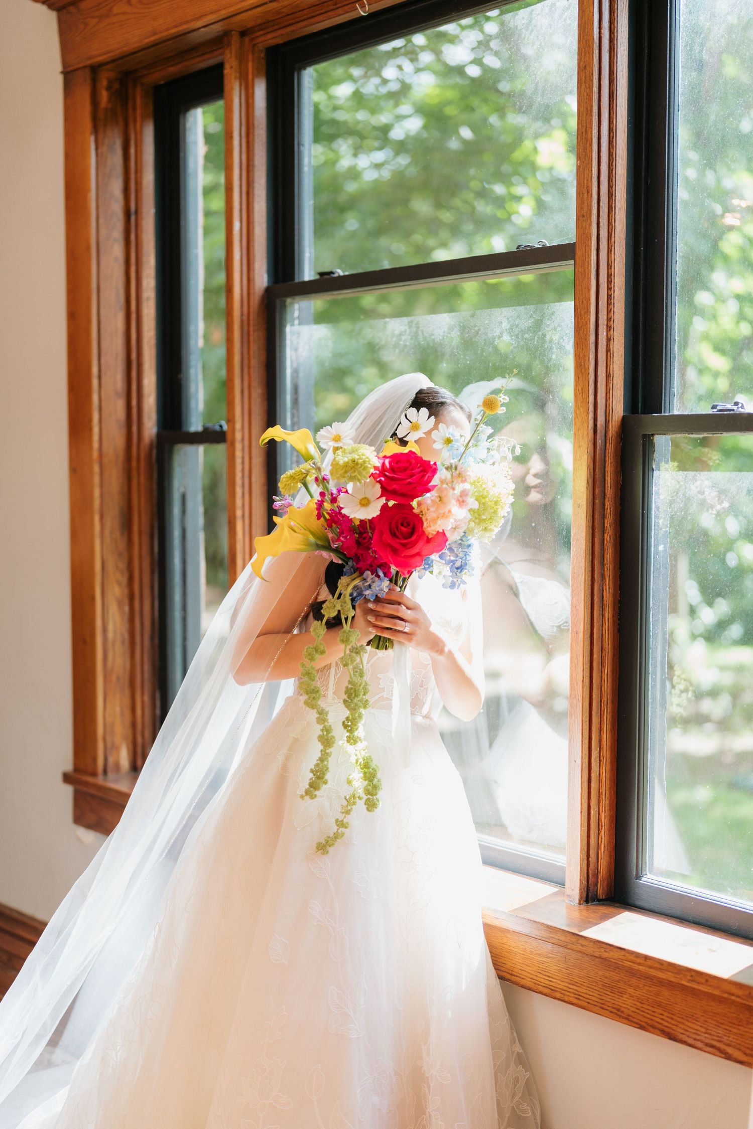 White wedding veil adorned with vibrant red and yellow floral arrangements displayed against sunlit windows.