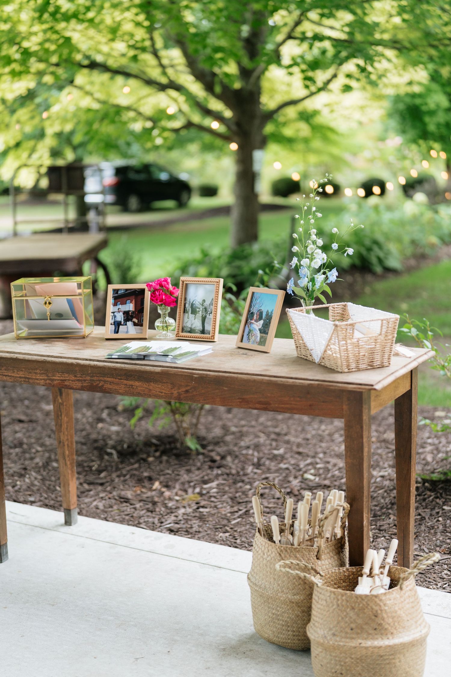 A rustic wooden table decorated with photo frames and woven baskets for a wedding guest book display outdoors.