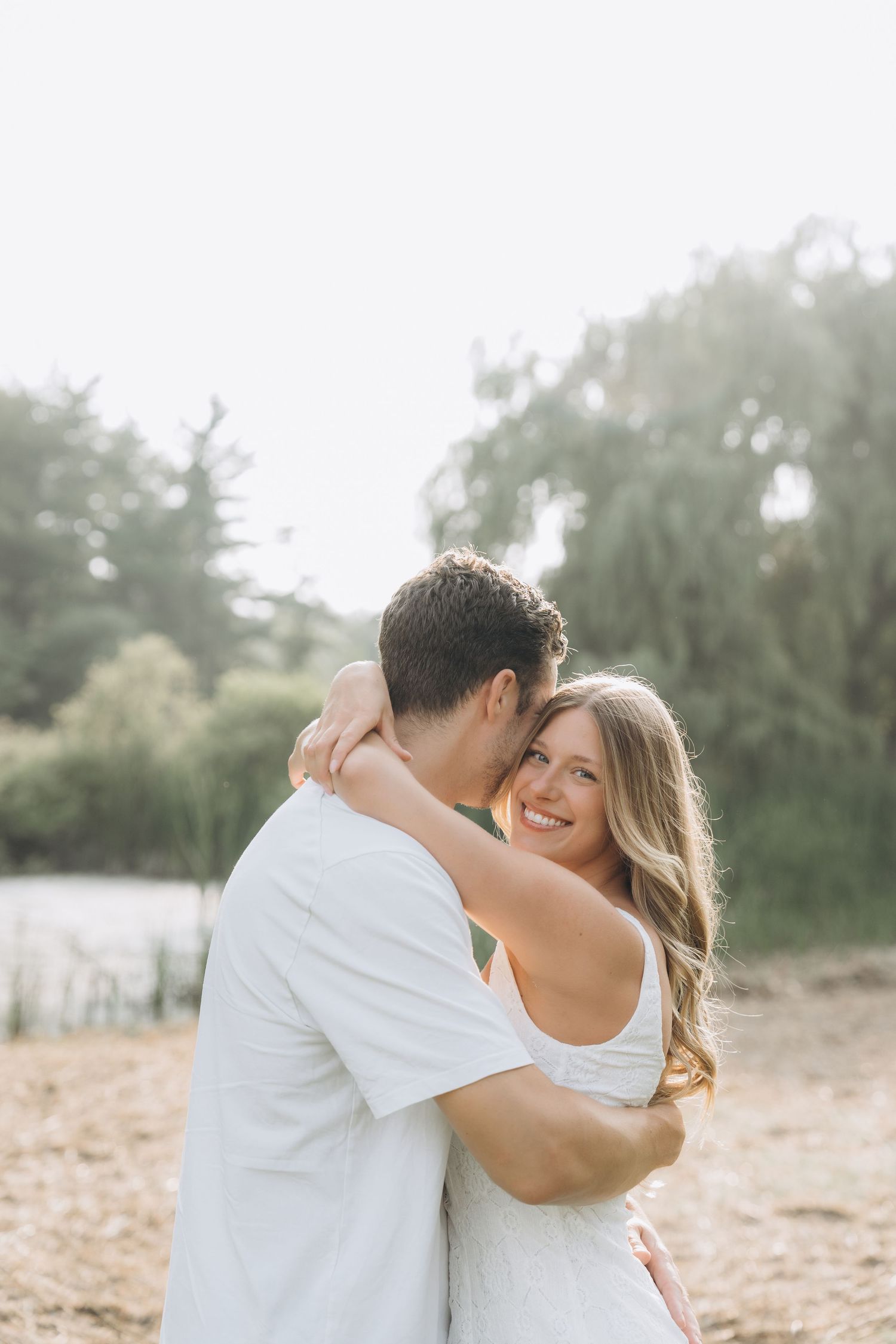 A couple embraces lovingly on a sandy beach path surrounded by greenery during a romantic photoshoot.