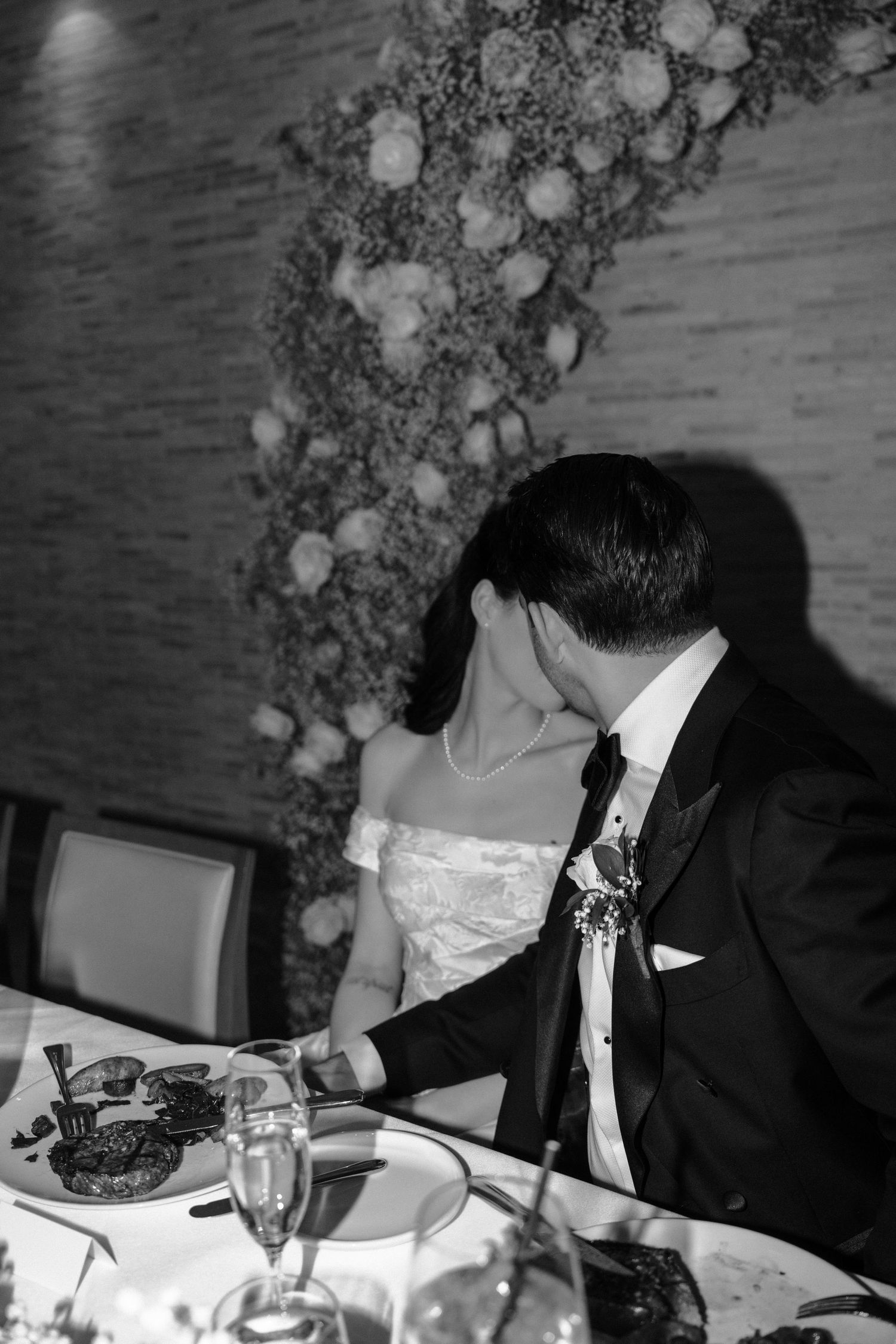 A black and white photograph of a formal dinner table setting with guests seated at a wedding reception.