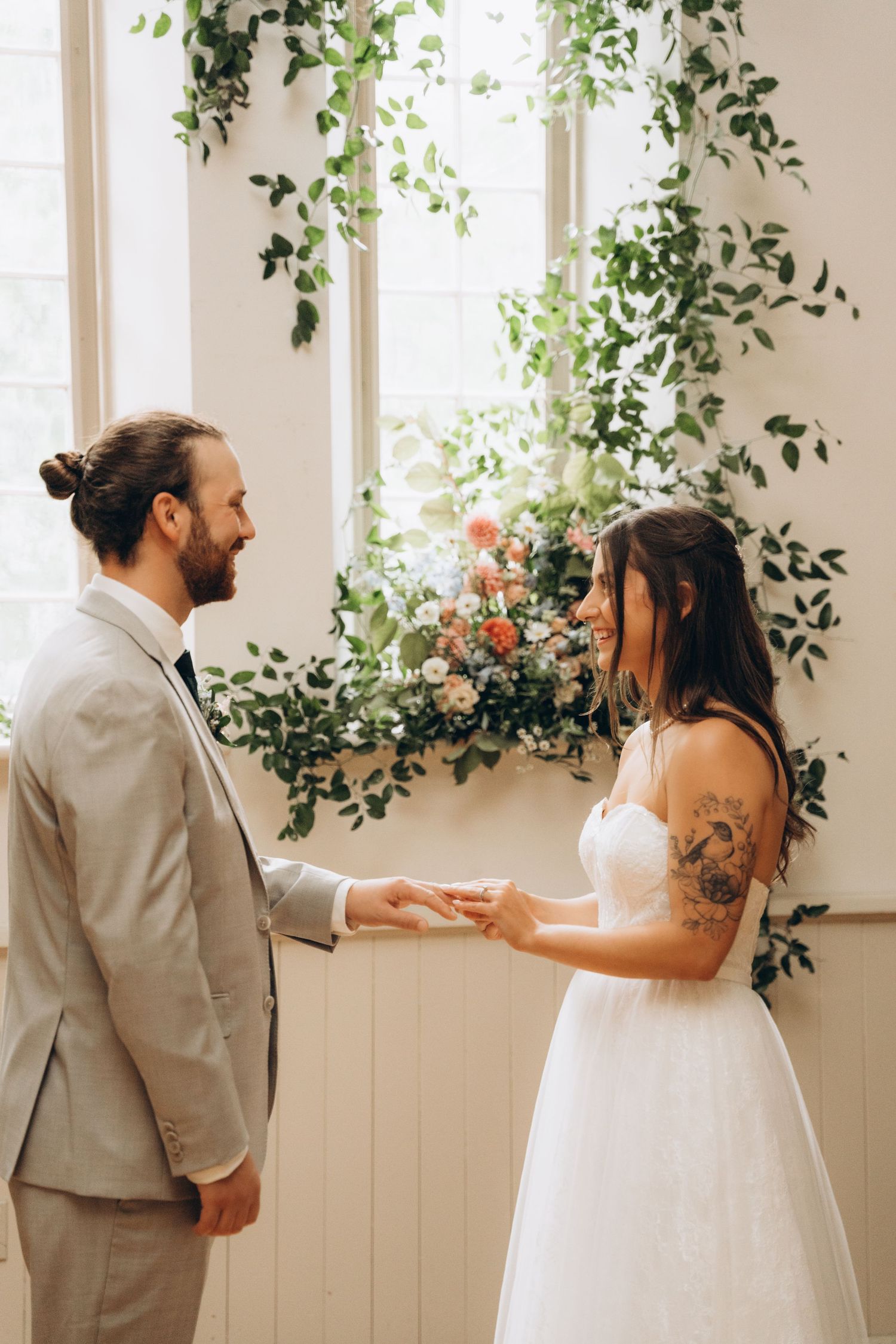 A first look wedding moment captured in a bright indoor space decorated with cascading greenery and windows.