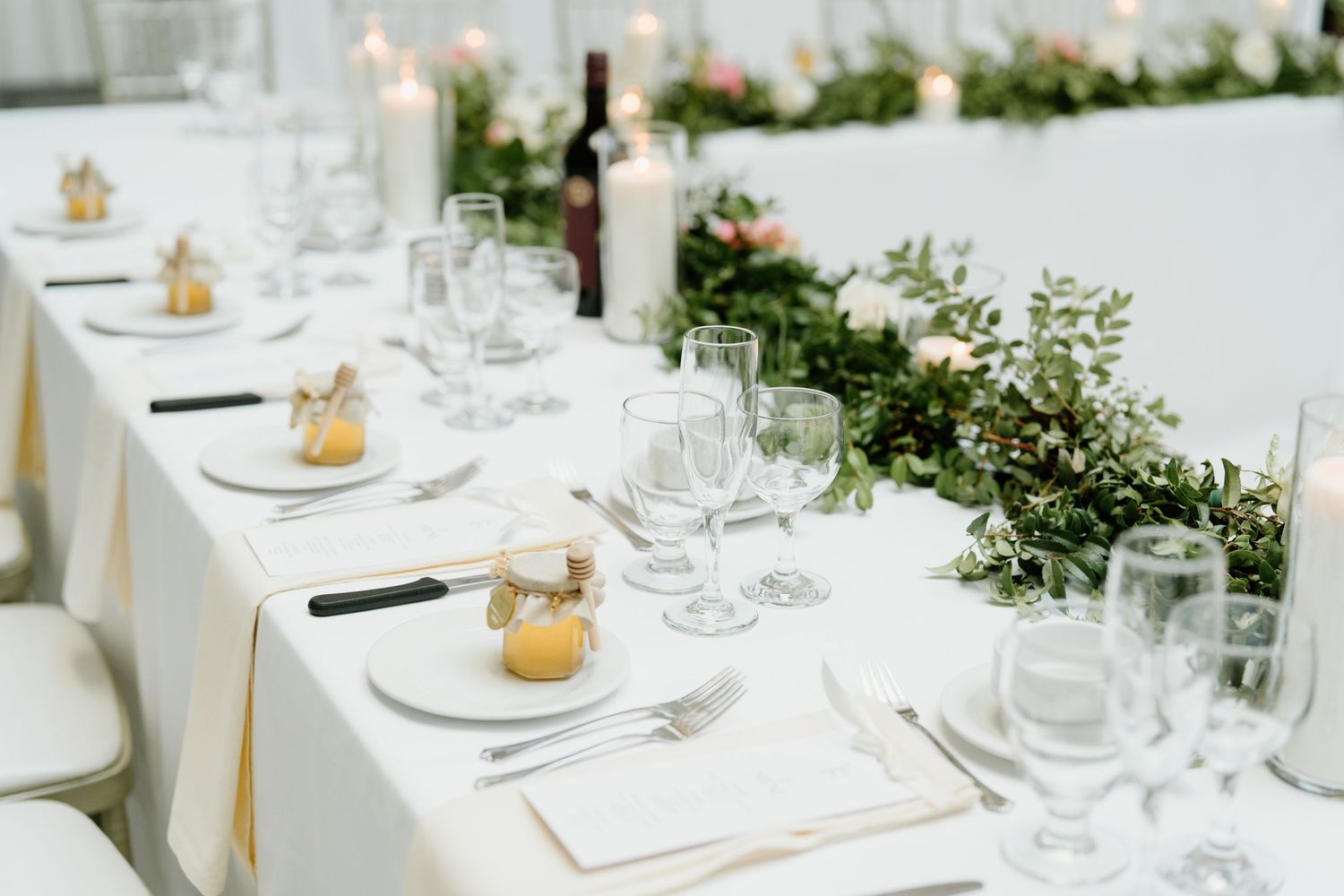 Elegant white wedding reception tables decorated with greenery garlands and small gold candle holders.