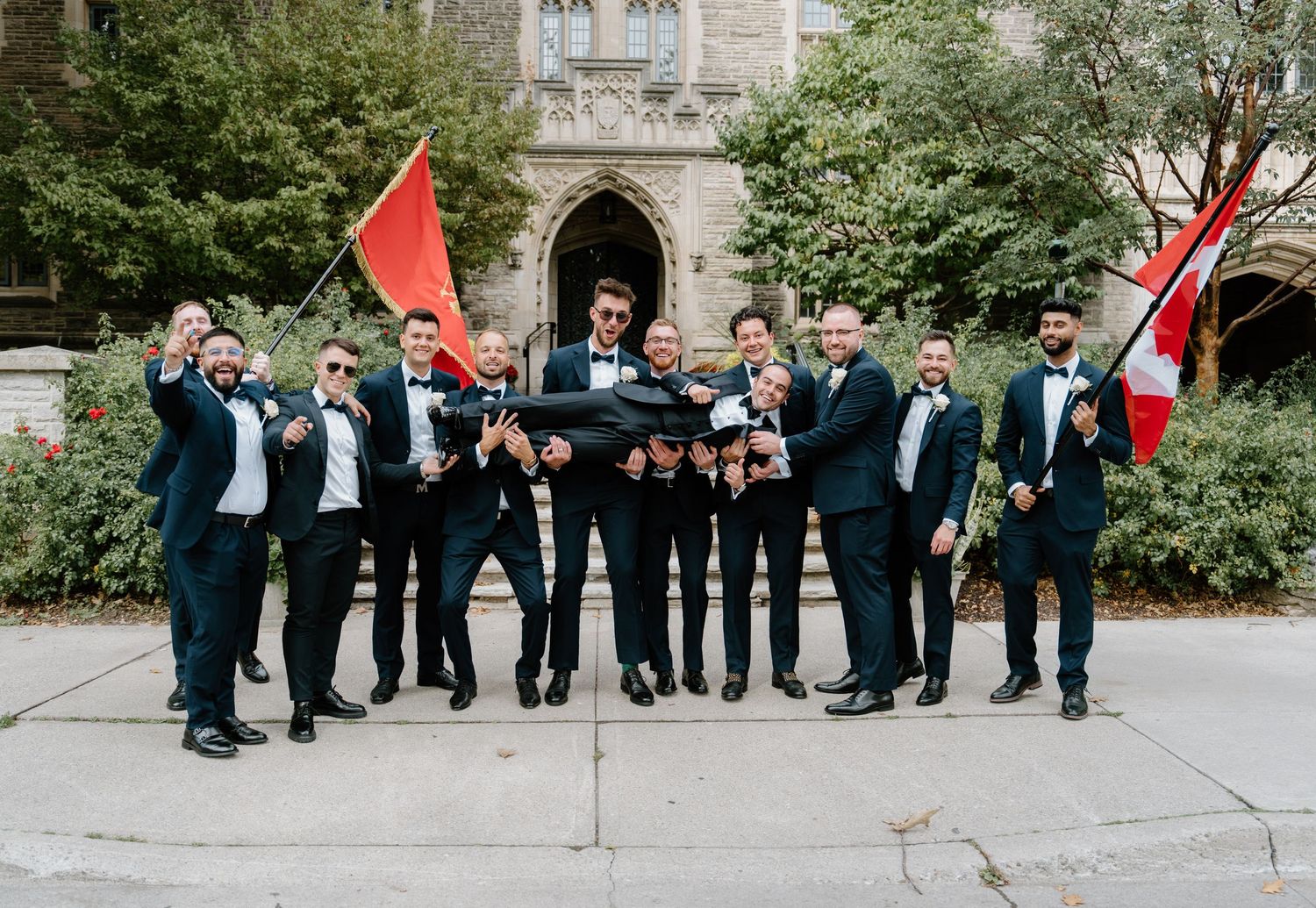 A group of formally dressed wedding guests stand in line outside a stone building during a ceremony.
