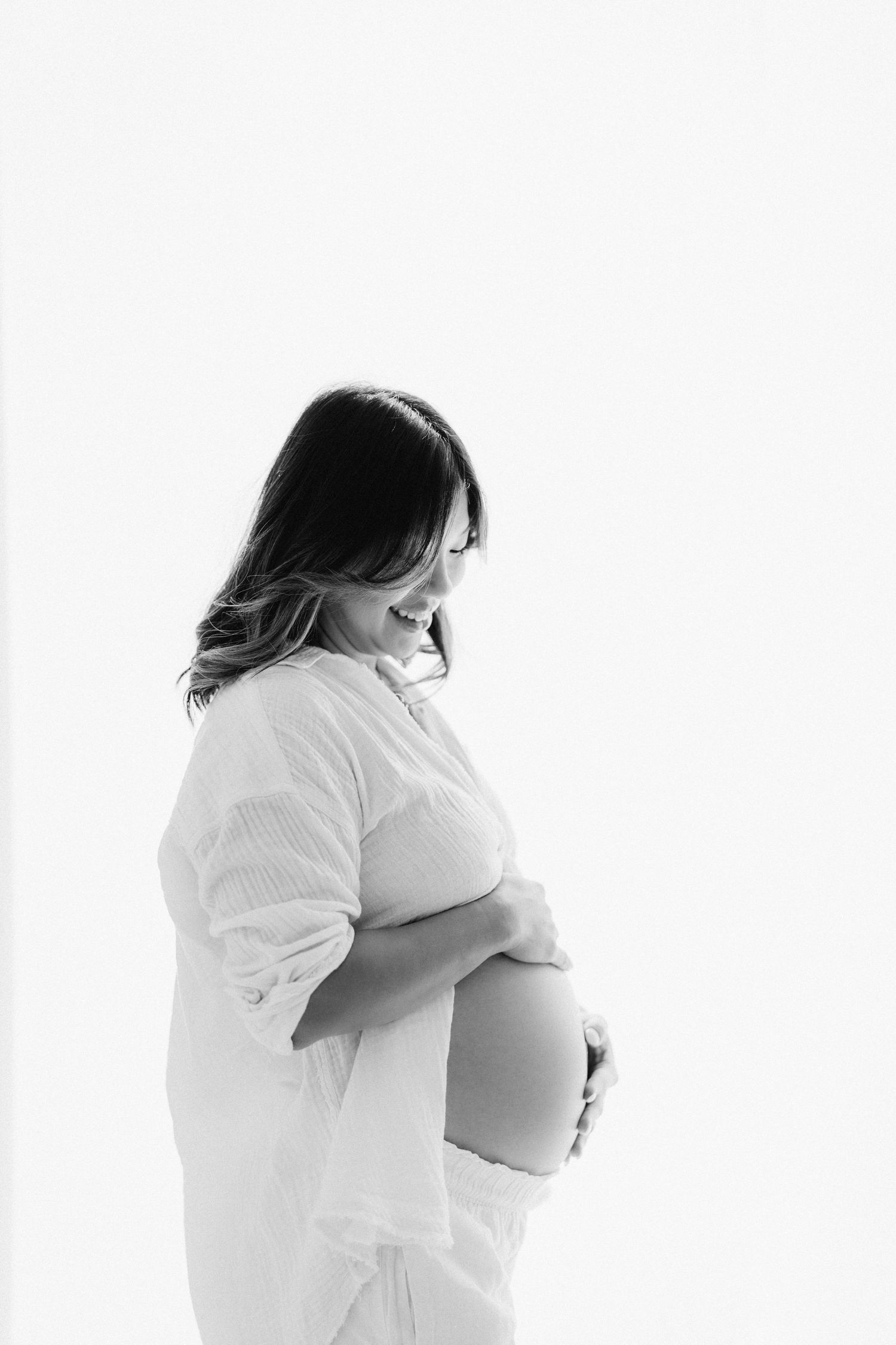 Three artistic black and white maternity photos show a woman in white clothing cradling her pregnant belly.