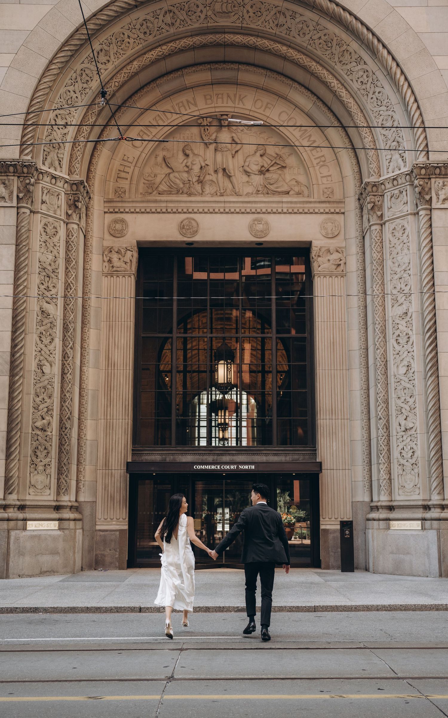 A couple entering an ornate stone building with grand archway and decorative architectural details.