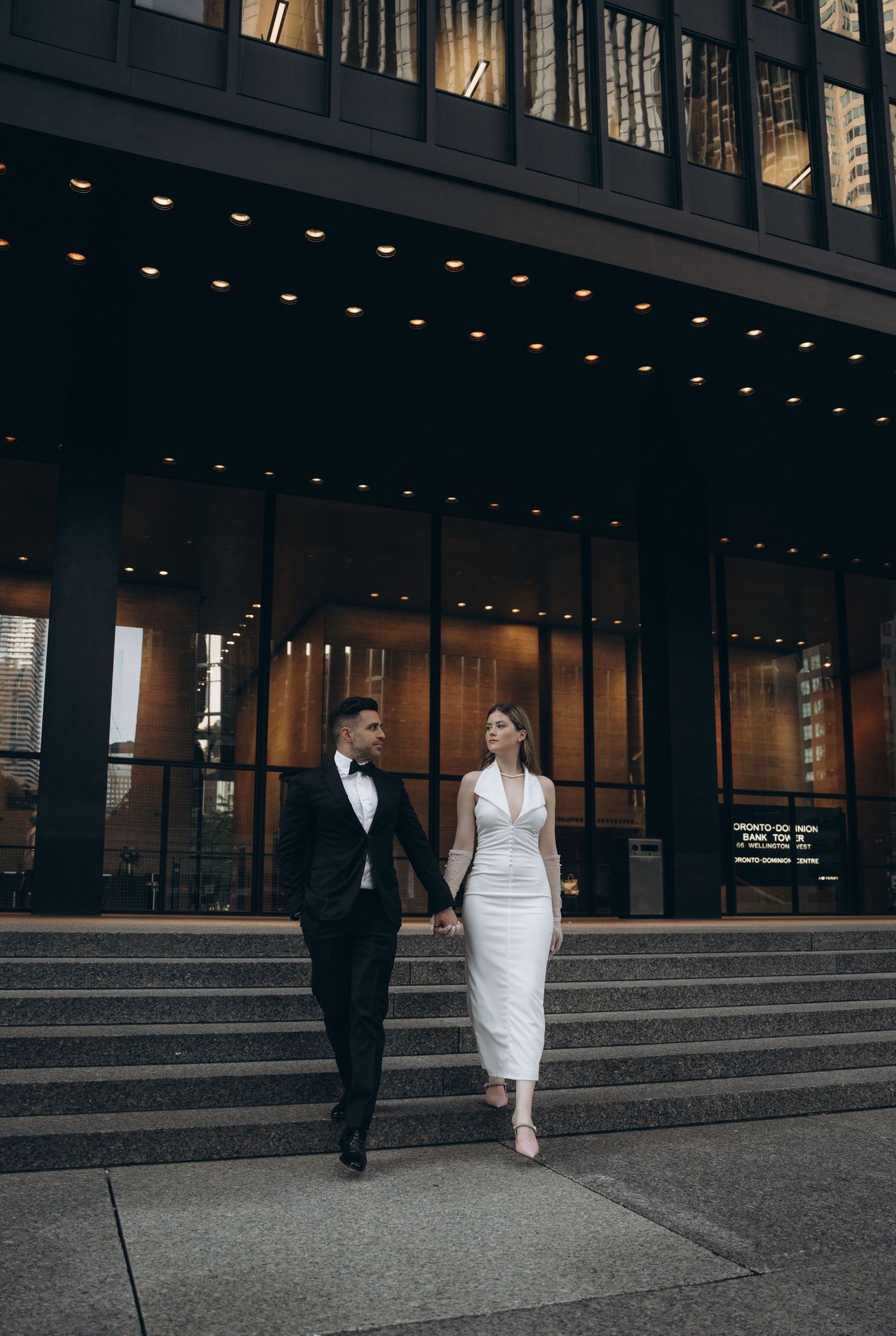 A couple walks along granite steps outside a modern commercial building with glass windows.