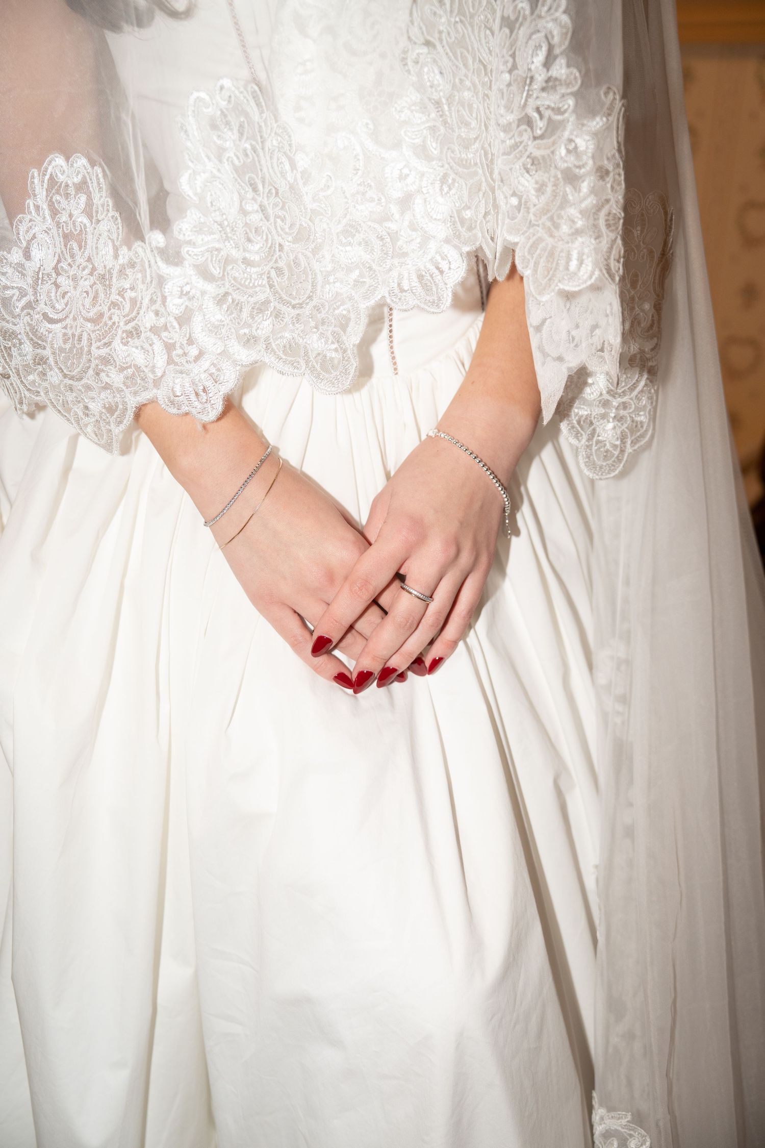 Close-up series of bridal hands with red nails against a white lace wedding dress showing wedding band details.