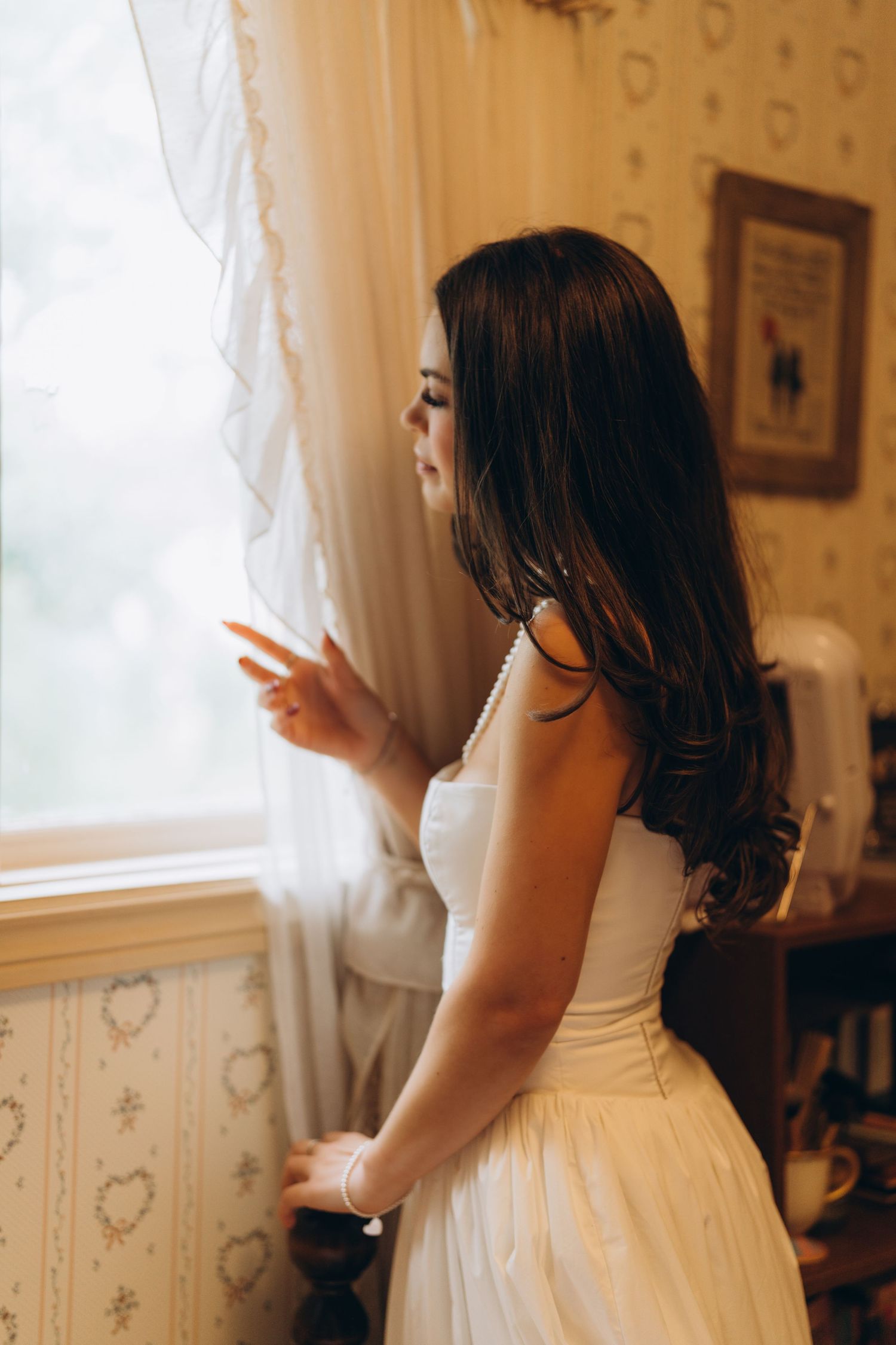 Wedding dress preparation scene with soft window light and delicate white details.